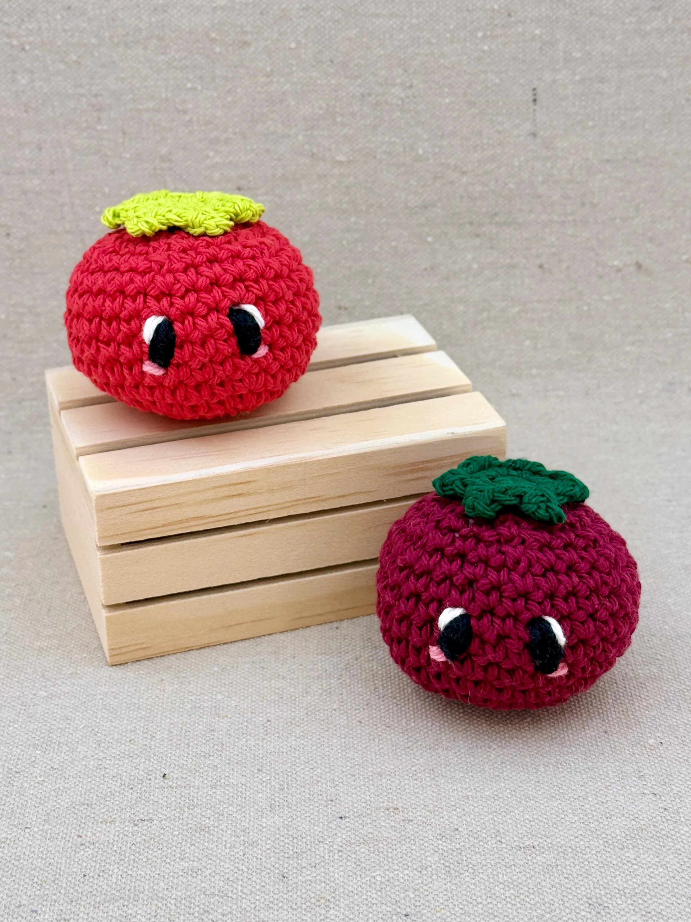 Two crochet amigurumi tomato plushies posed with a mini wooden crate in red and burgundy (Copy)