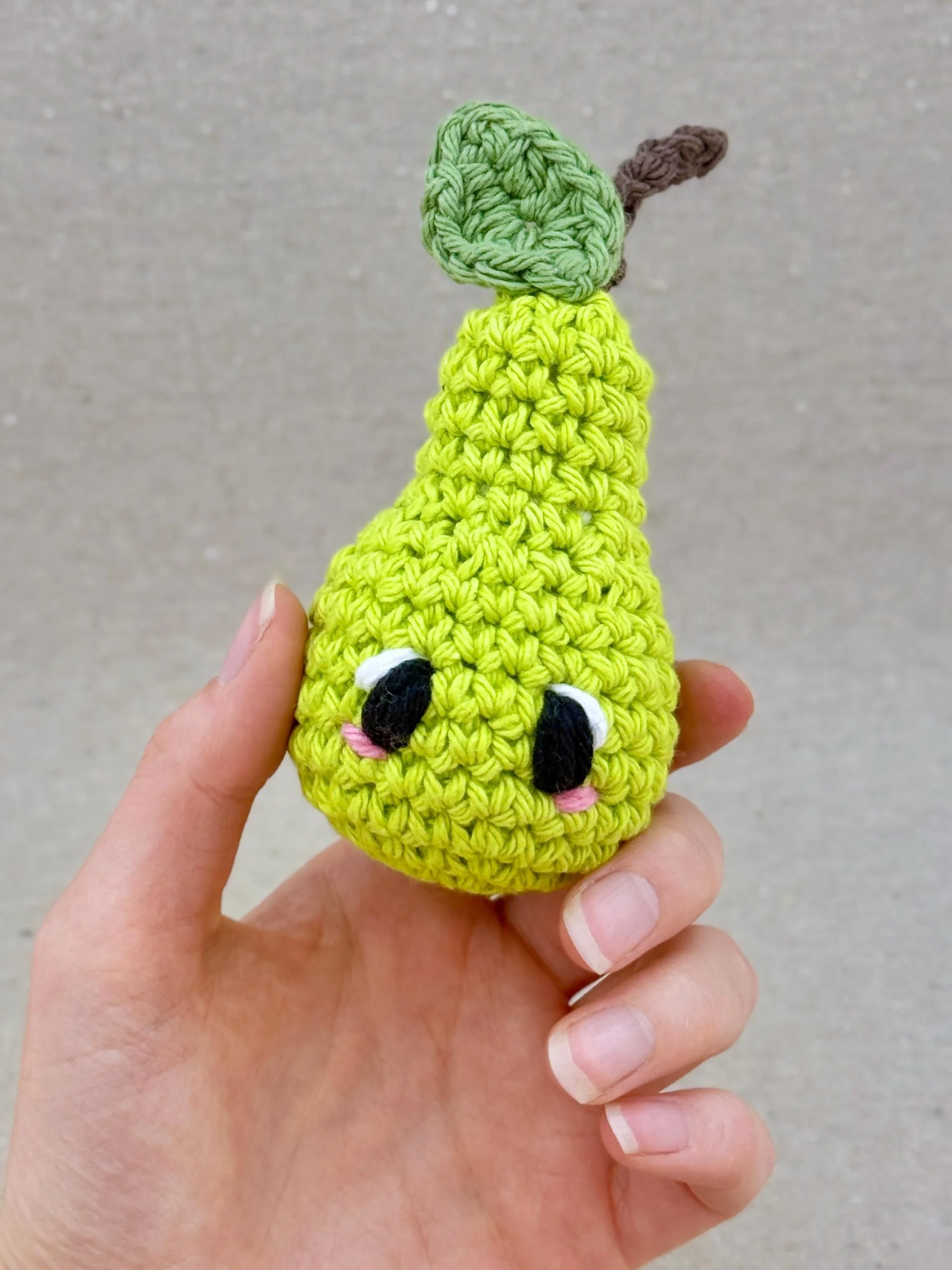 A lime green crochet pear plush held in a hand (Copy)