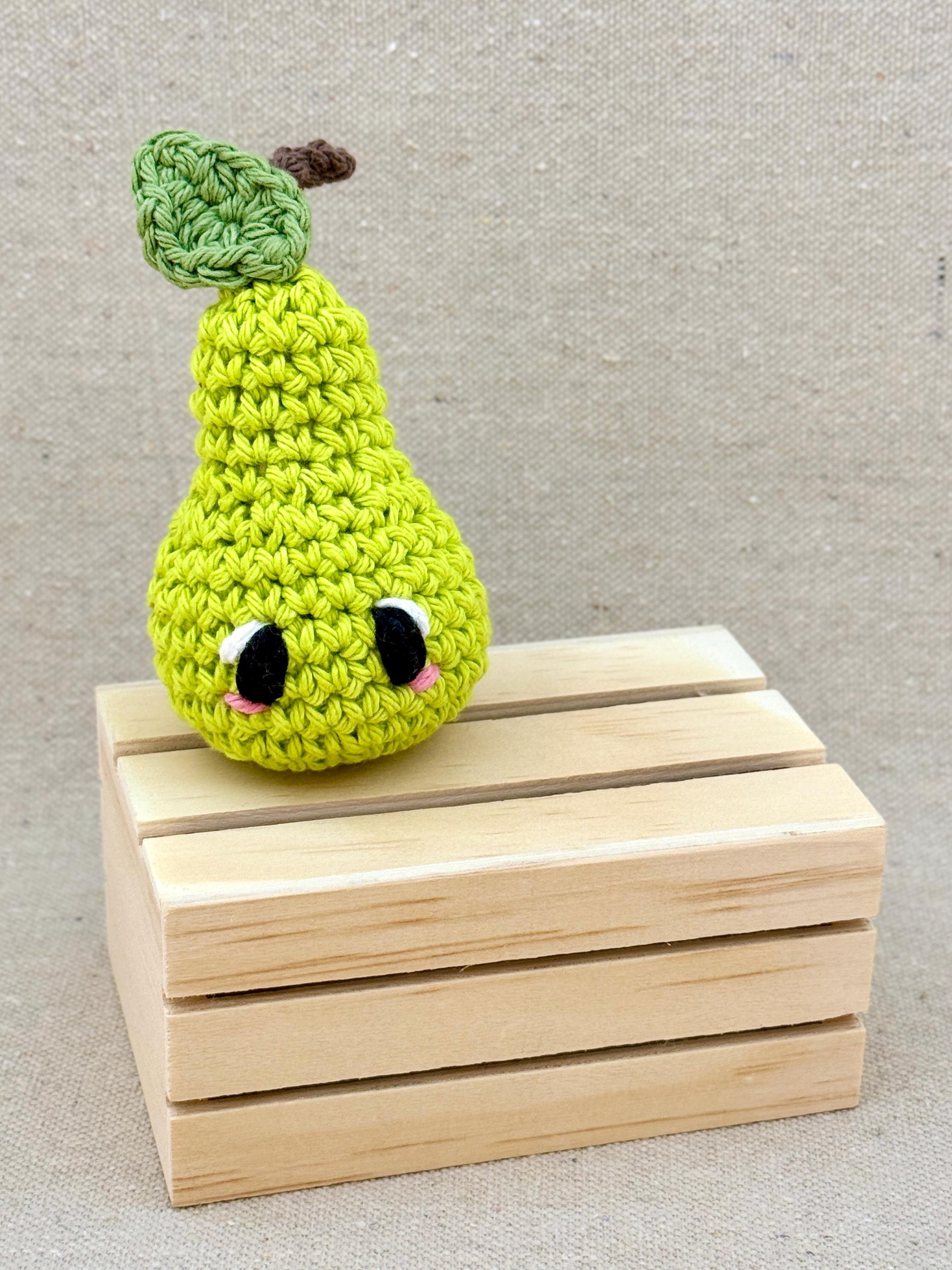 A lime green amigurumi pear plush posed with a mini wooden crate (Copy)