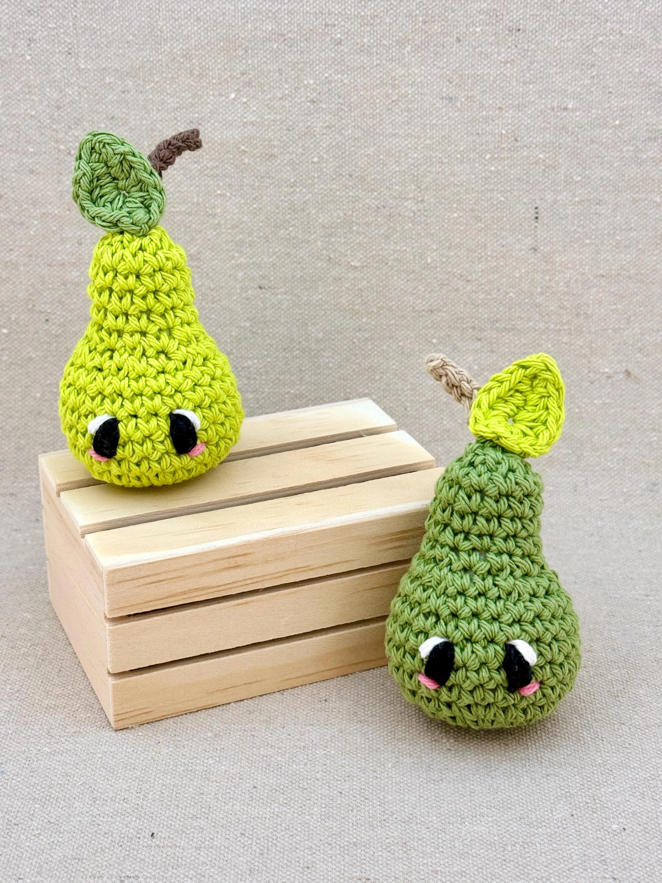 Two crochet amigurumi pear plushies posed with a mini wooden crate in lime green and sage green (Copy)