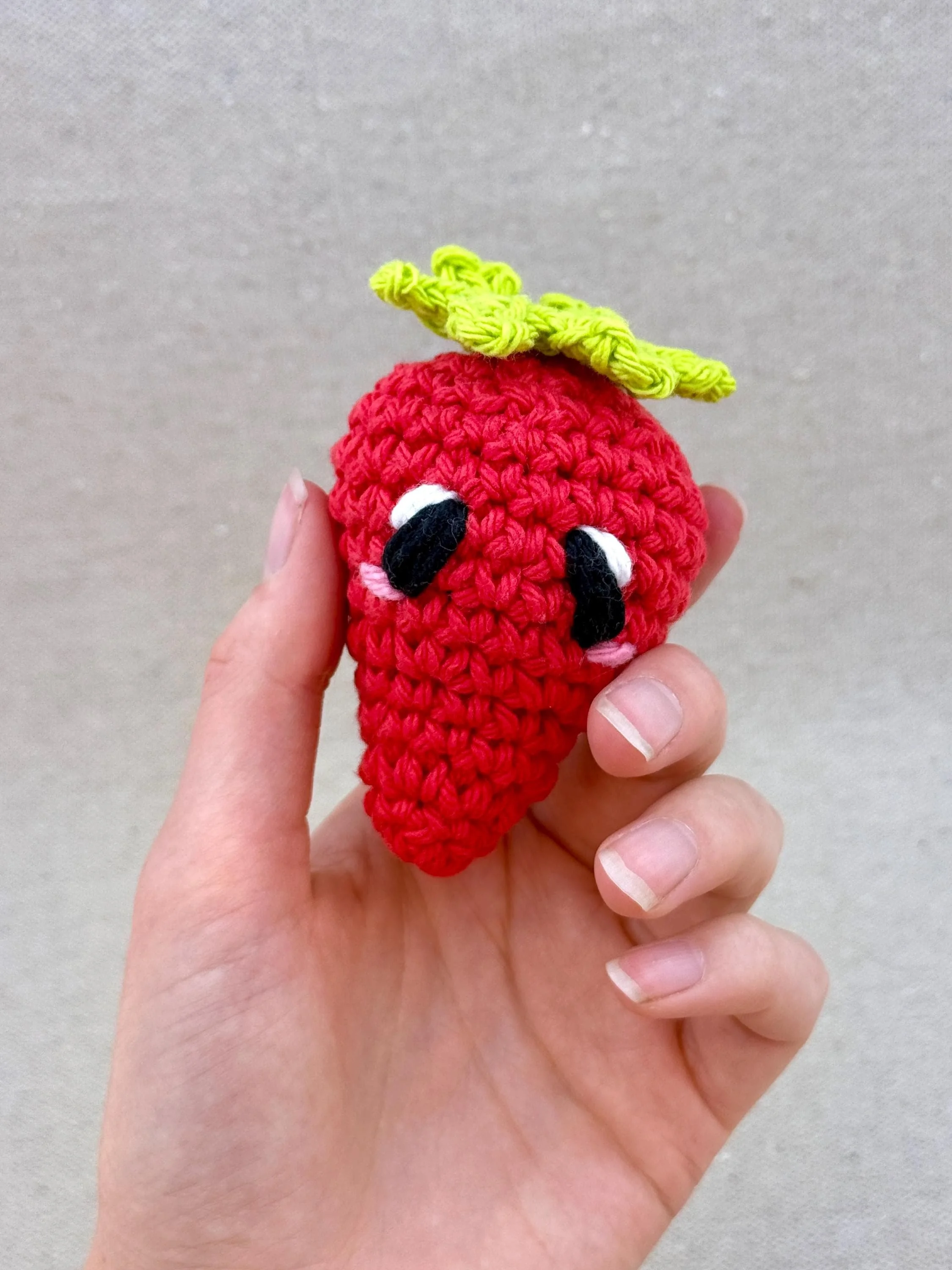 A red crochet strawberry plush held in a hand (Copy)
