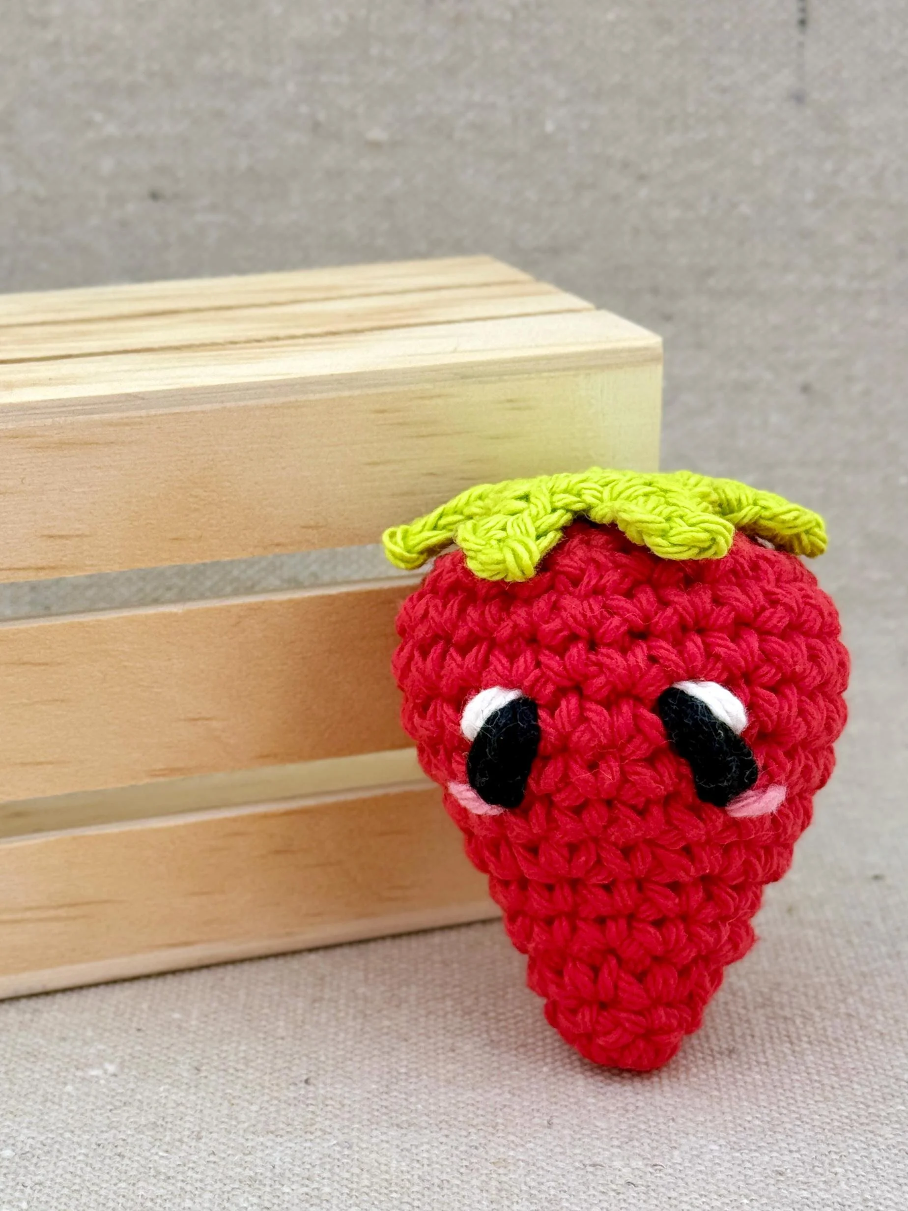 A red amigurumi strawberry plush posed with a mini wooden crate (Copy)