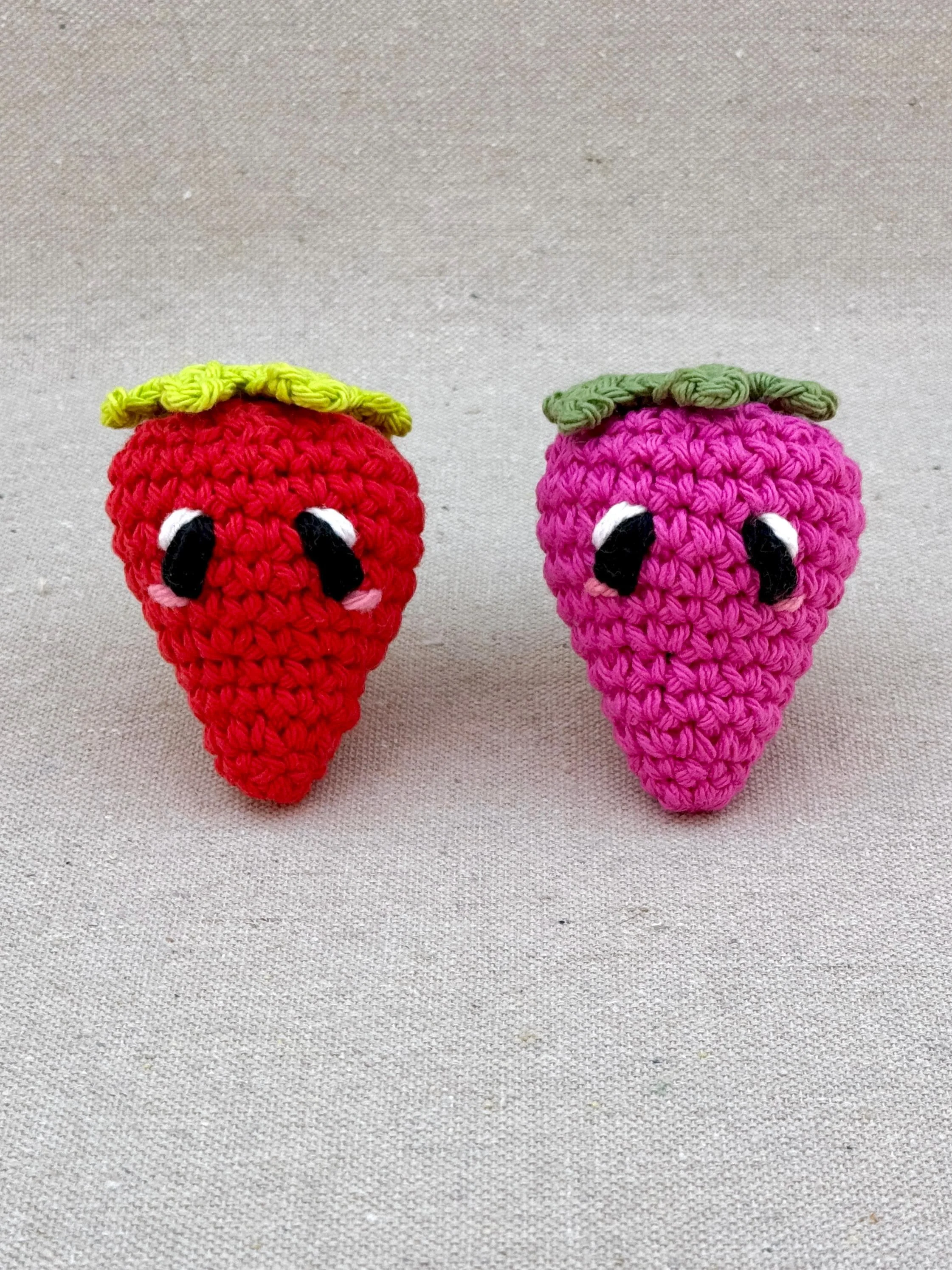 Two crochet strawberries in red and hot pink sitting next to each other (Copy)