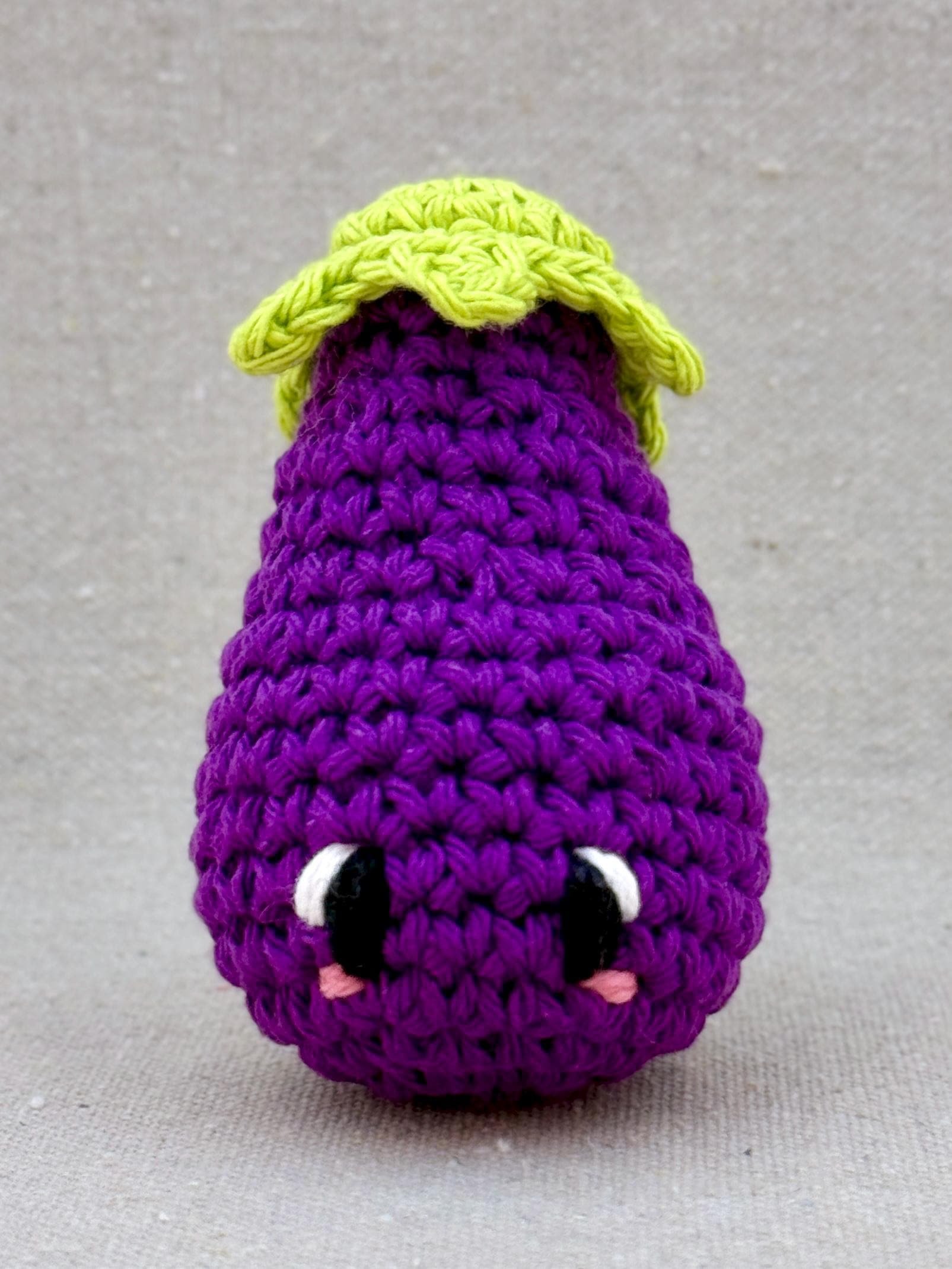 Close up of a dark purple eggplant amigurumi plush made from cotton yarn and cotton stuffing