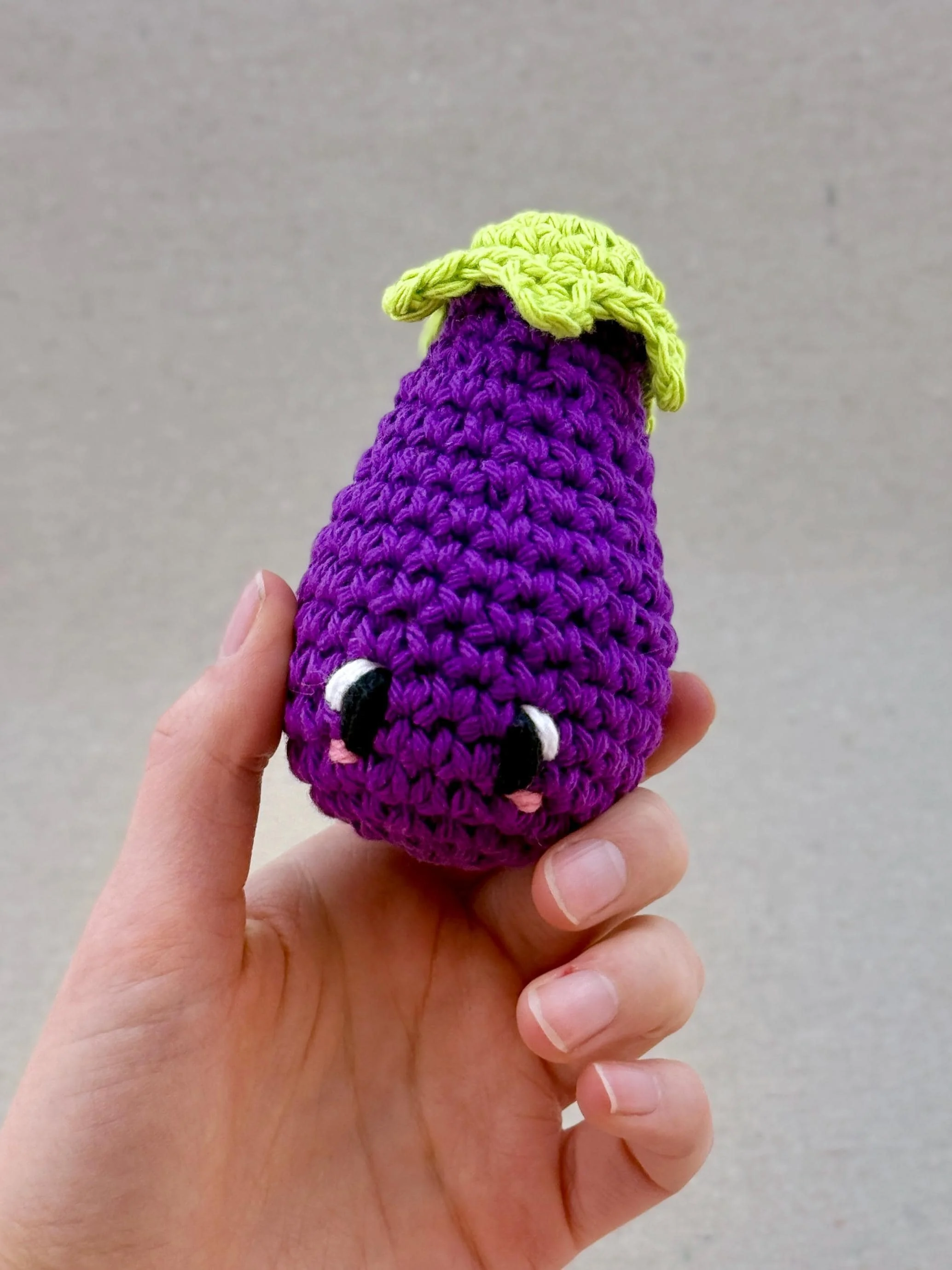 A dark purple crochet eggplant plush held in a hand
