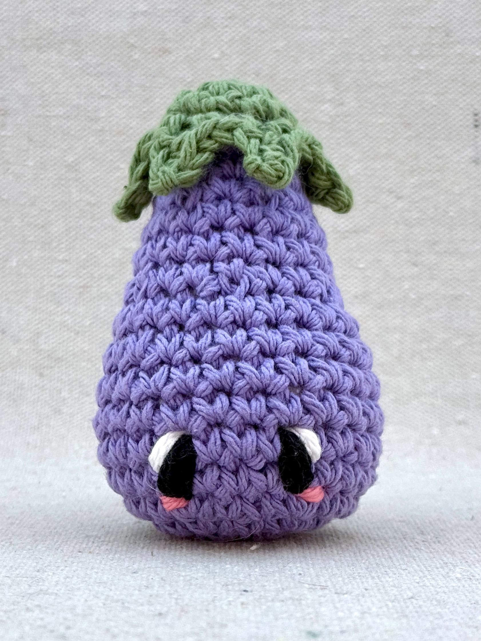 Close up of a light purple eggplant amigurumi plush made from cotton yarn and cotton stuffing