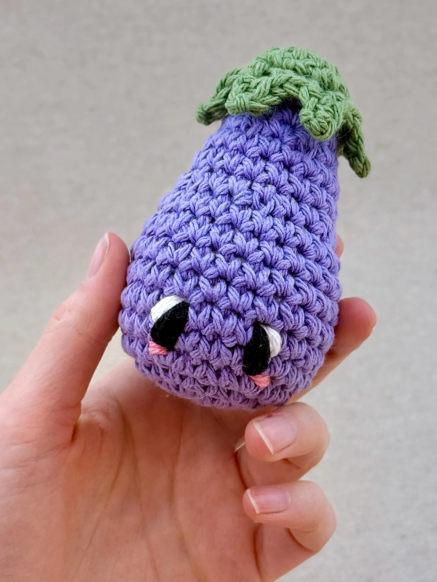 A light purple crochet eggplant plush held in a hand