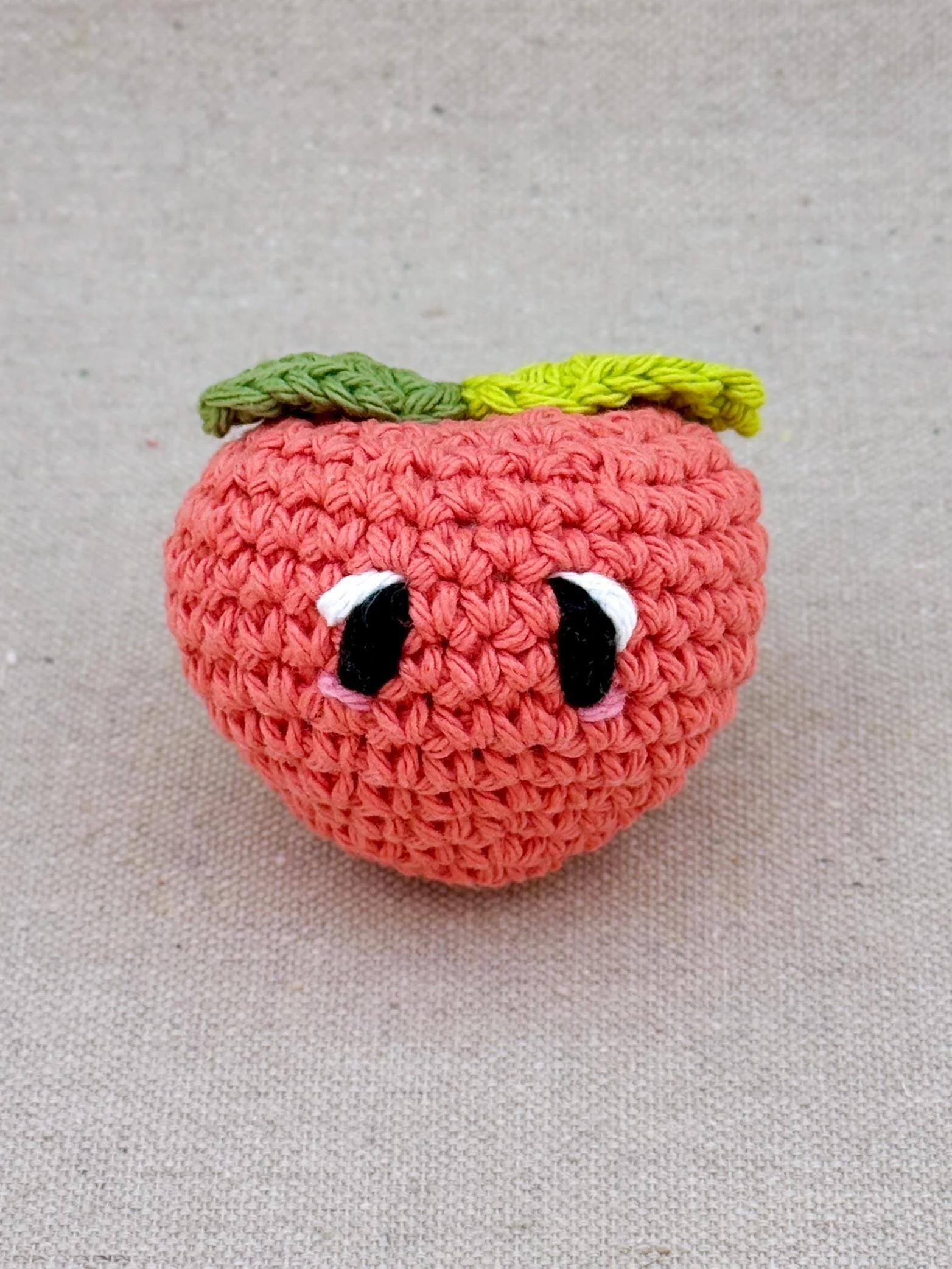 Close up of a coral peach amigurumi plush made from cotton yarn and cotton stuffing