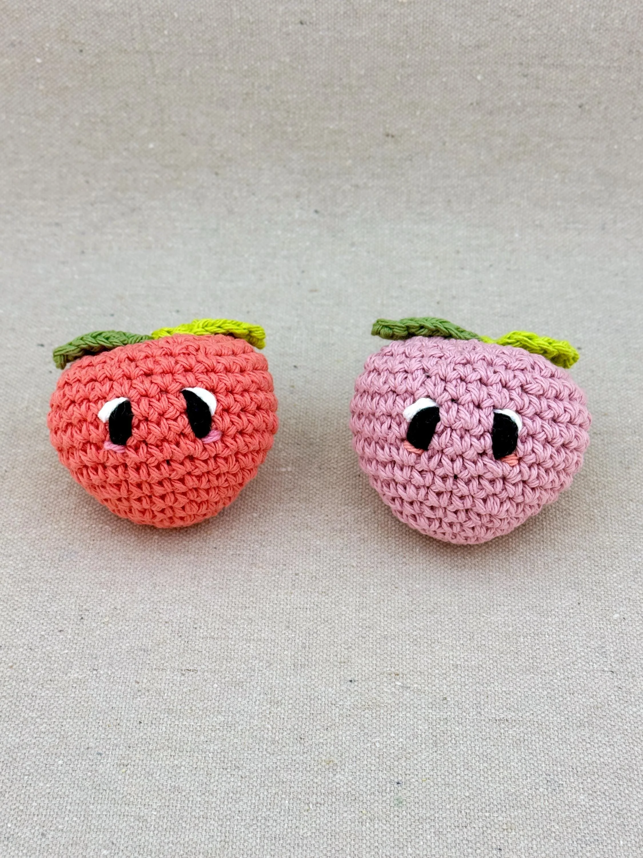 Two crochet peaches in coral and bubblegum sitting next to each other