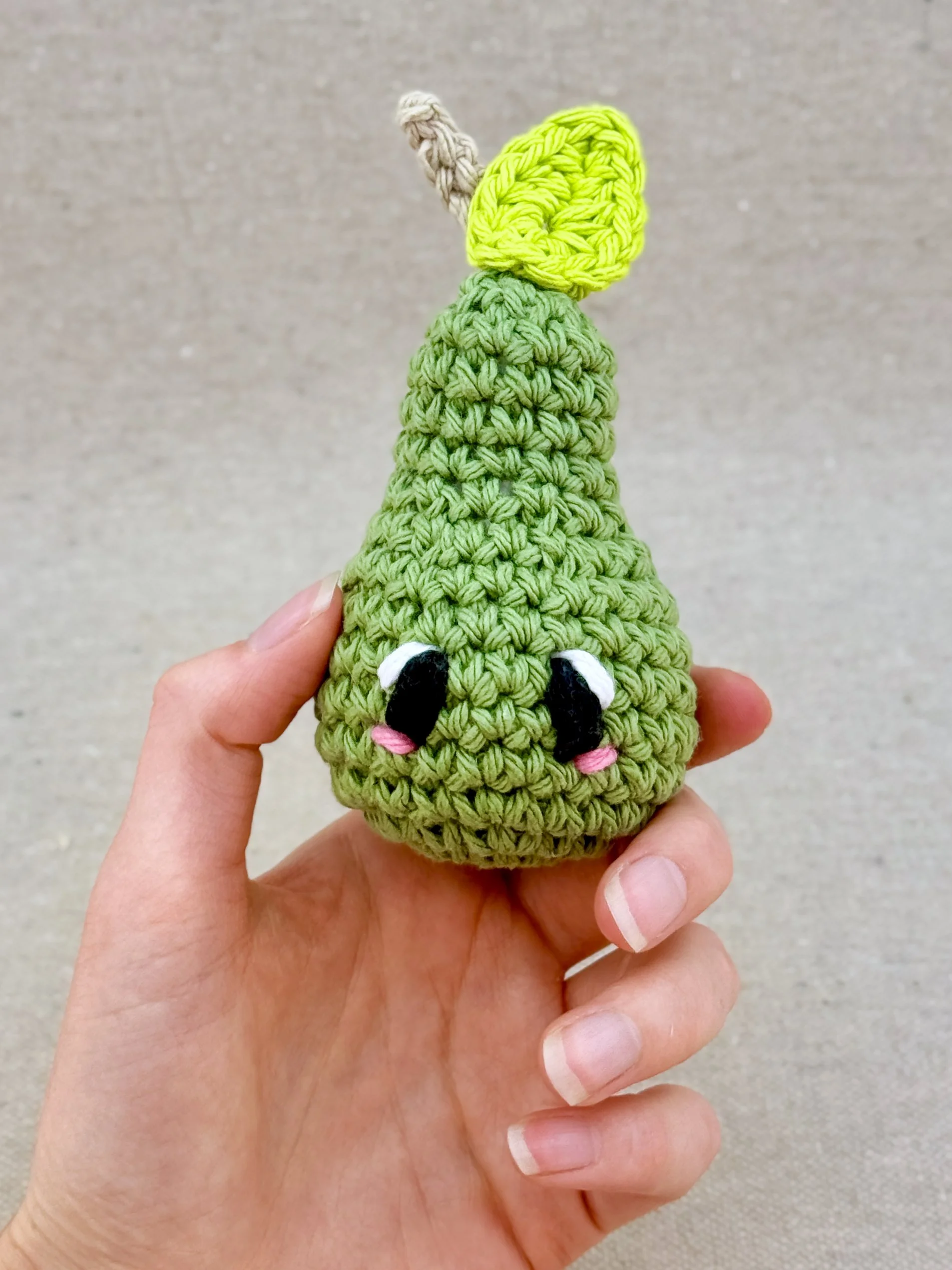 A sage green crochet pear plush held in a hand (Copy)