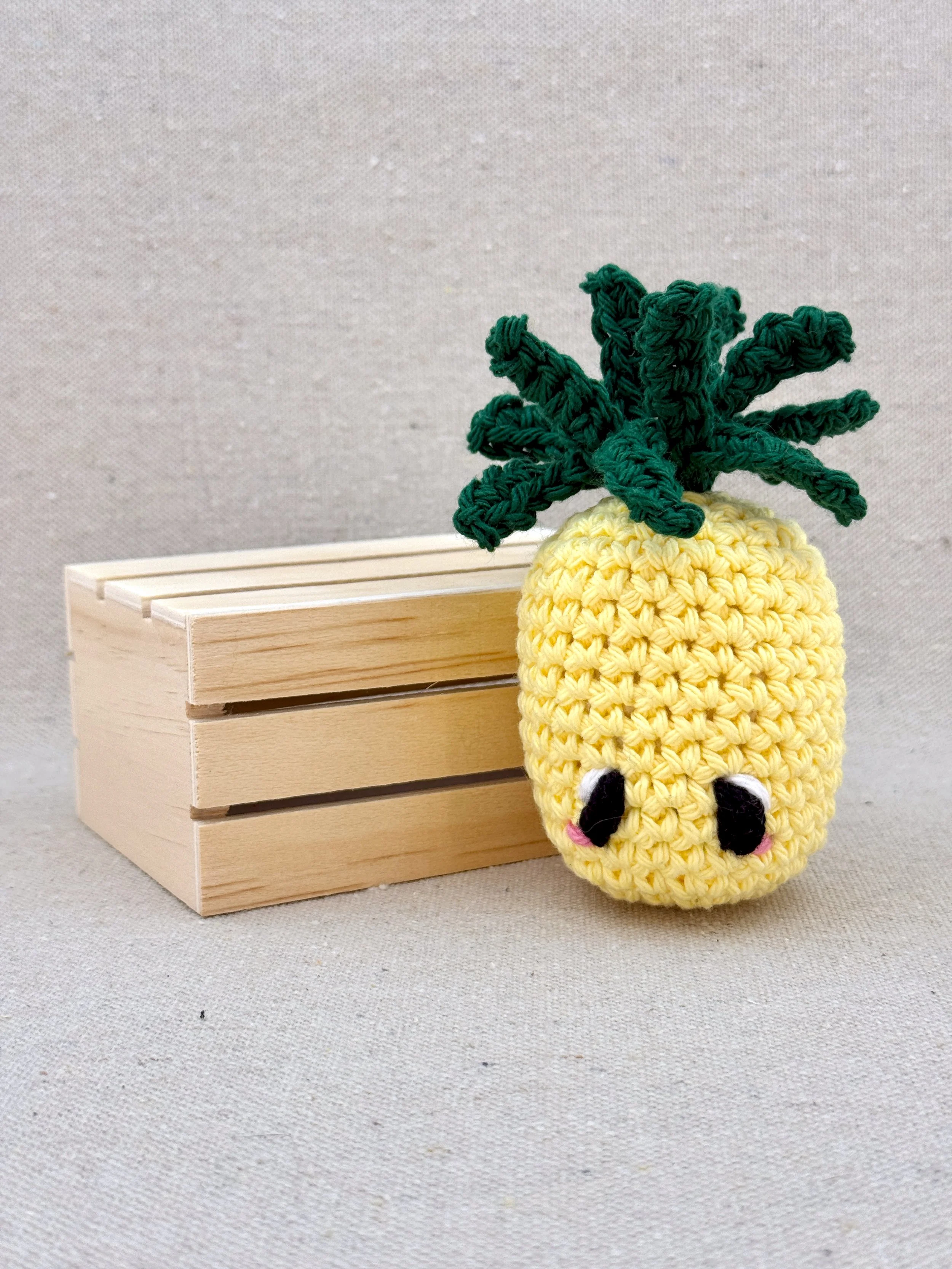 A butter yellow amigurumi pineapple plush posed with a mini wooden crate (Copy)