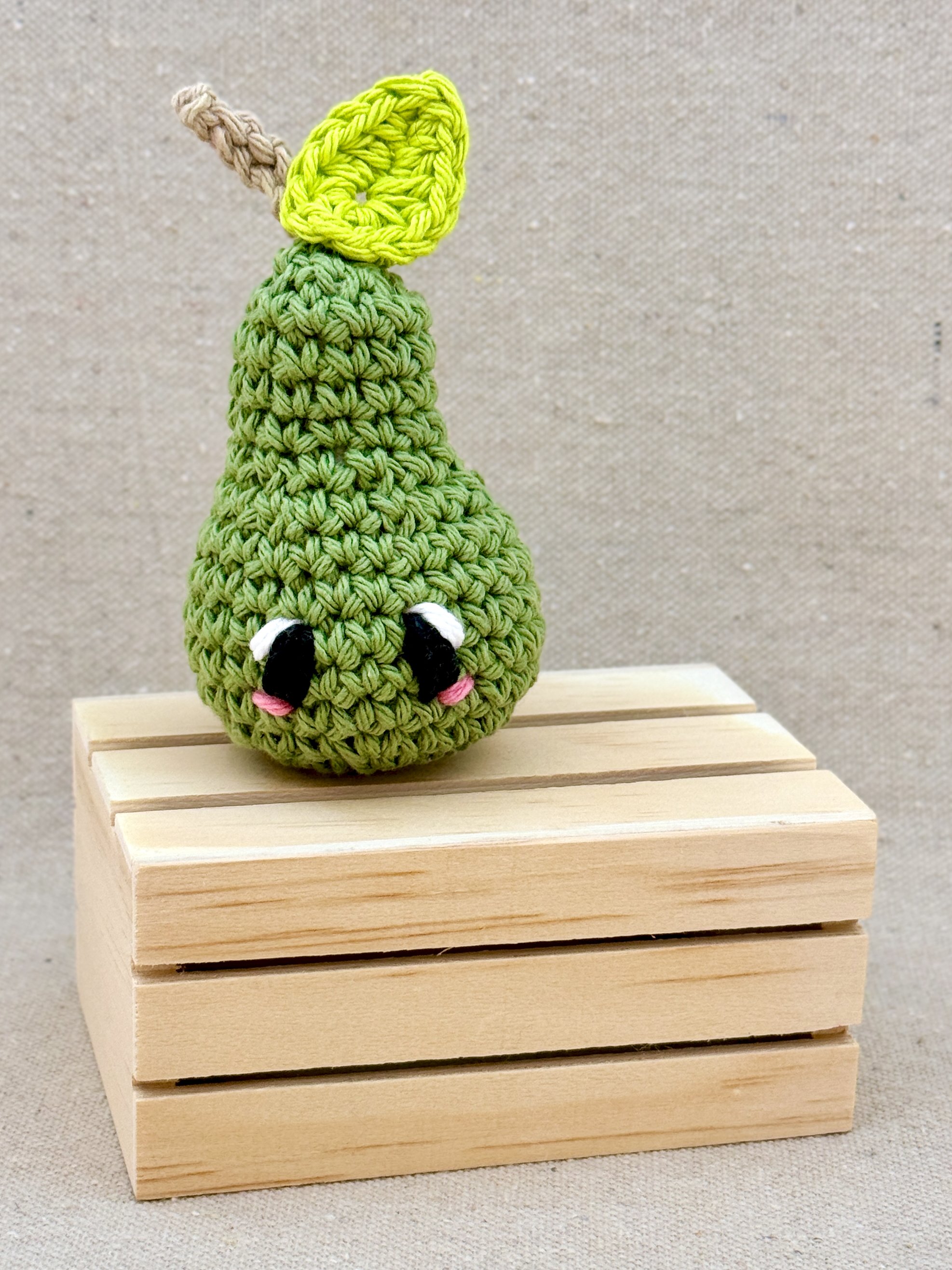 A sage green amigurumi pear plush posed with a mini wooden crate (Copy)