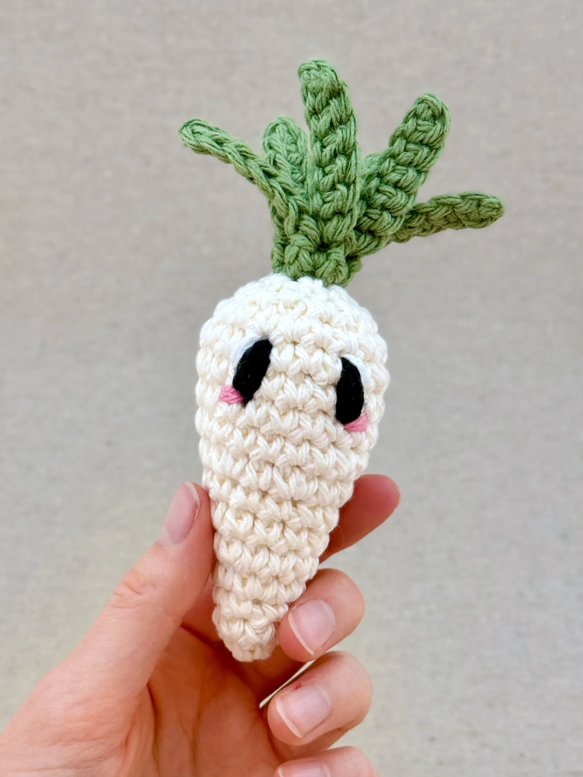 A cream crochet carrot plush held in a hand (Copy)