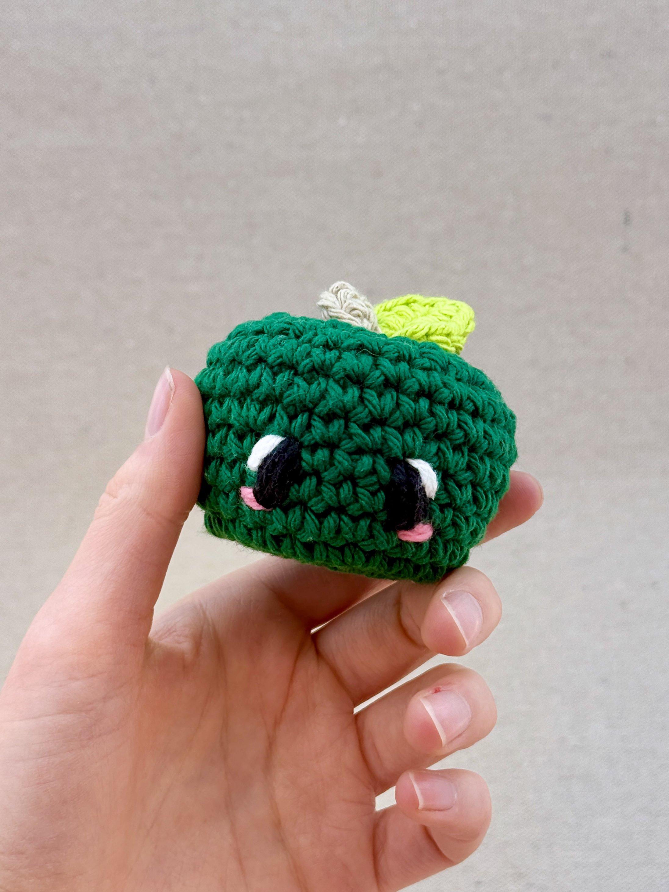 A pine green crochet apple plush held in a hand