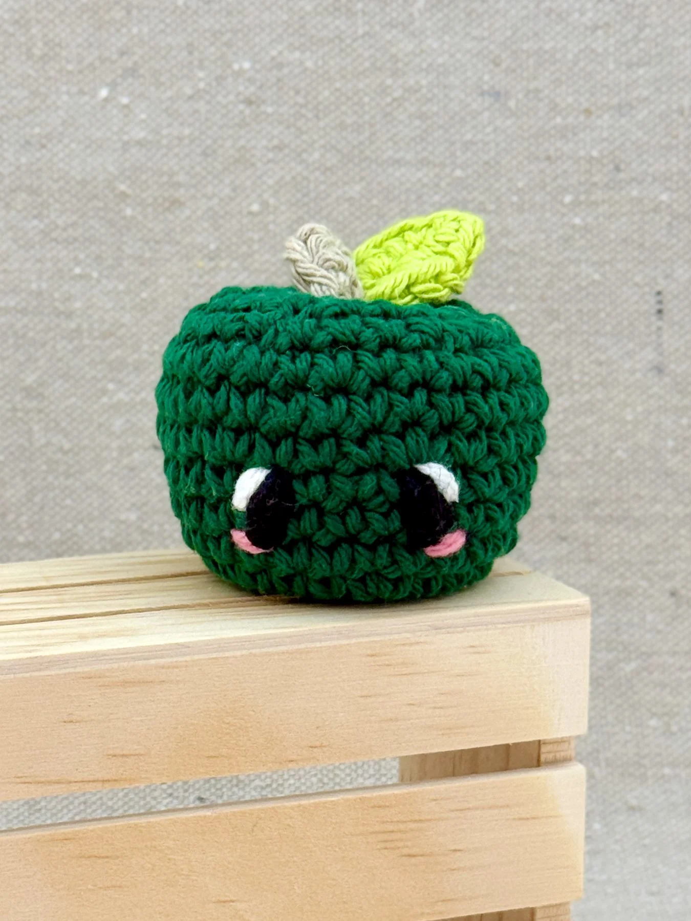 A pine green amigurumi apple plush posed with a mini wooden crate
