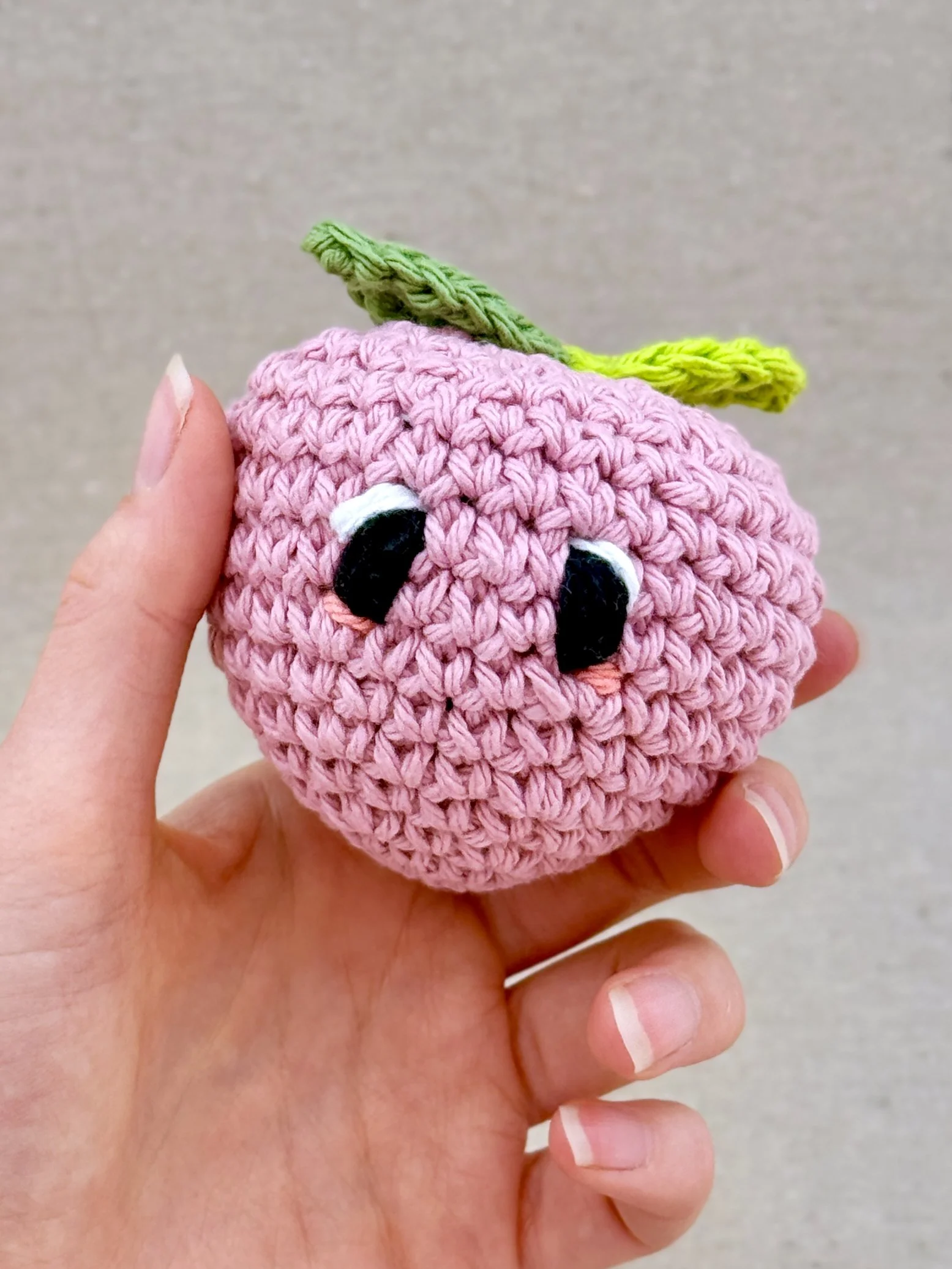 A bubblegum crochet peach plush held in a hand