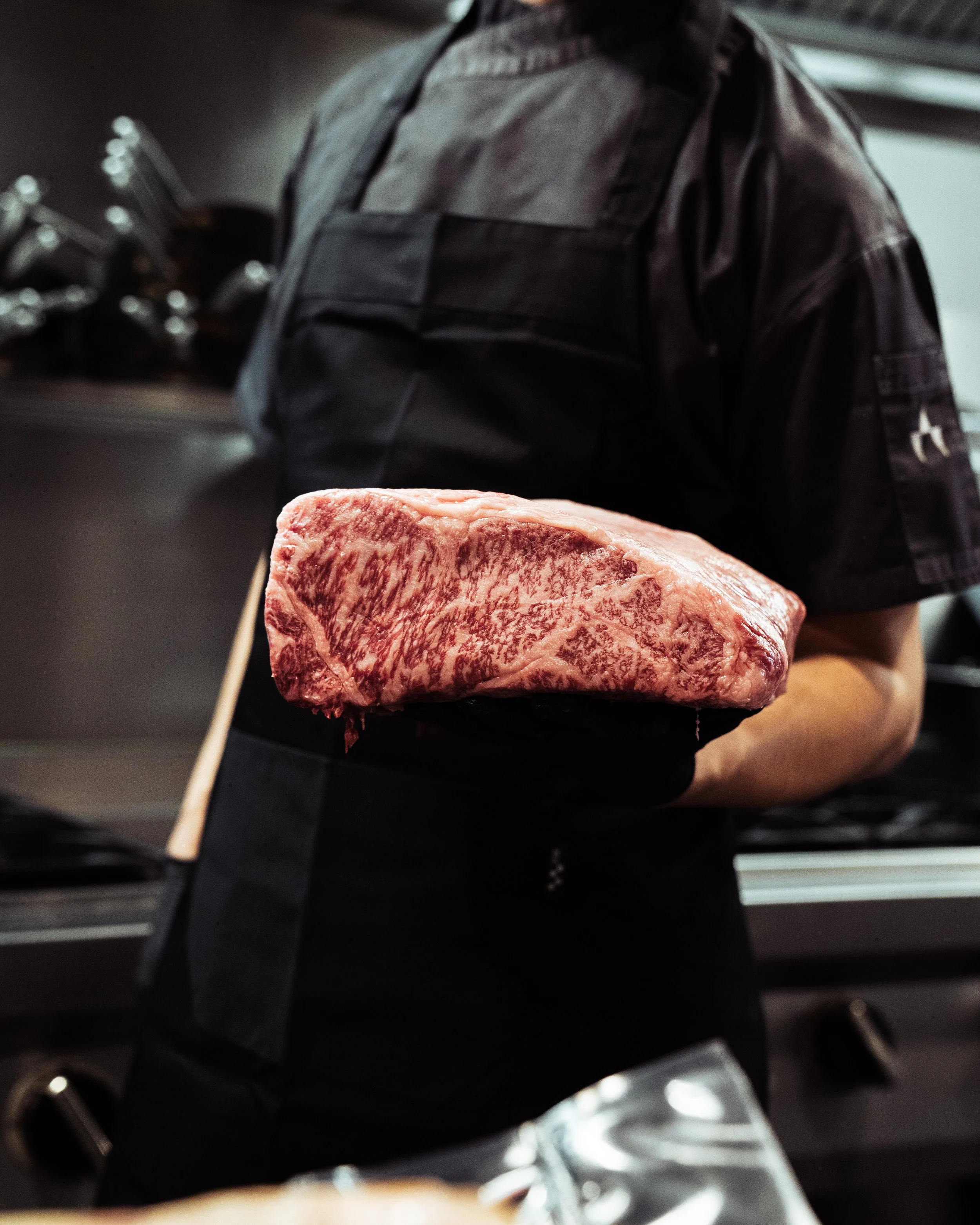 Persoon die een stuk gemarmerd rood vlees vasthoudt in een keuken.