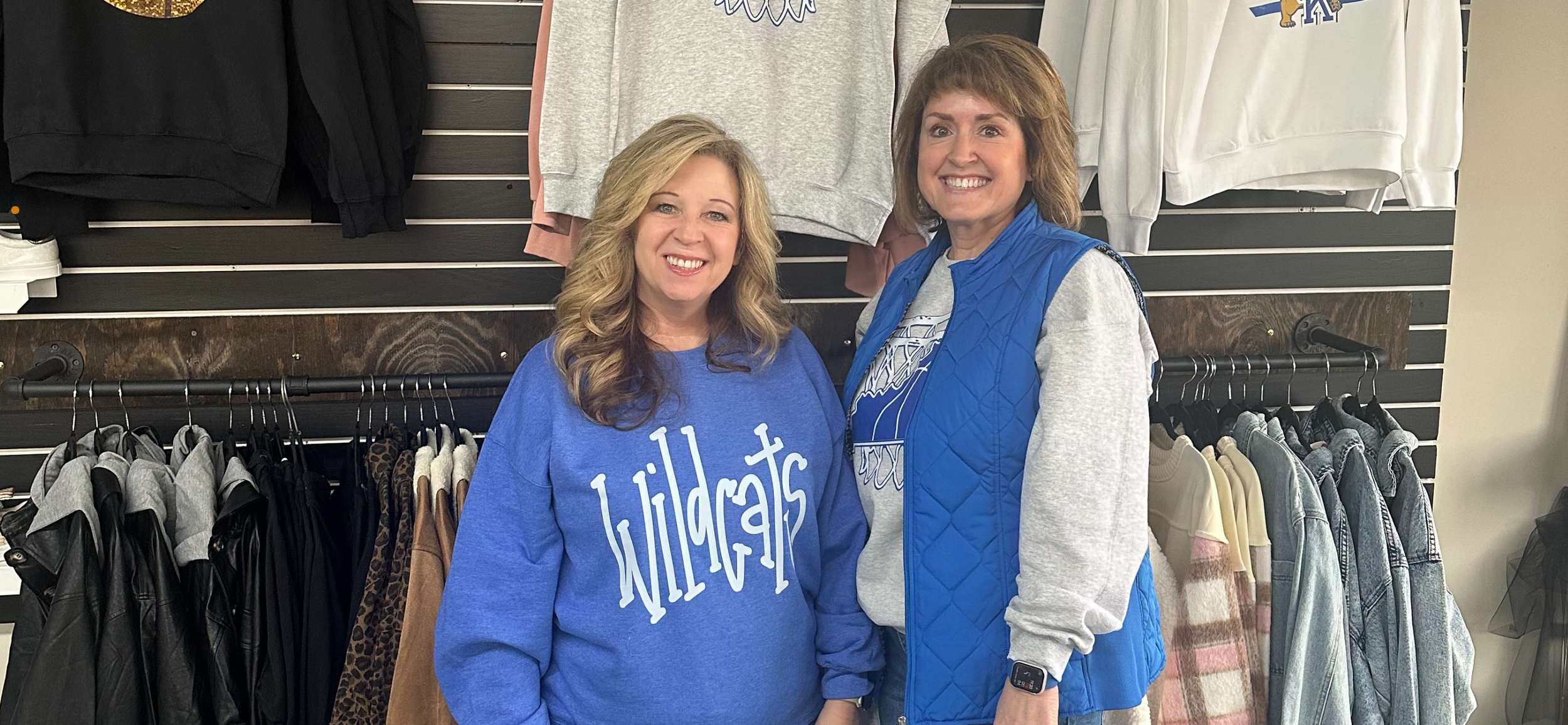 Owner and Store Manager, standing in front of racks of shirts and jackets. Slay the Day!
