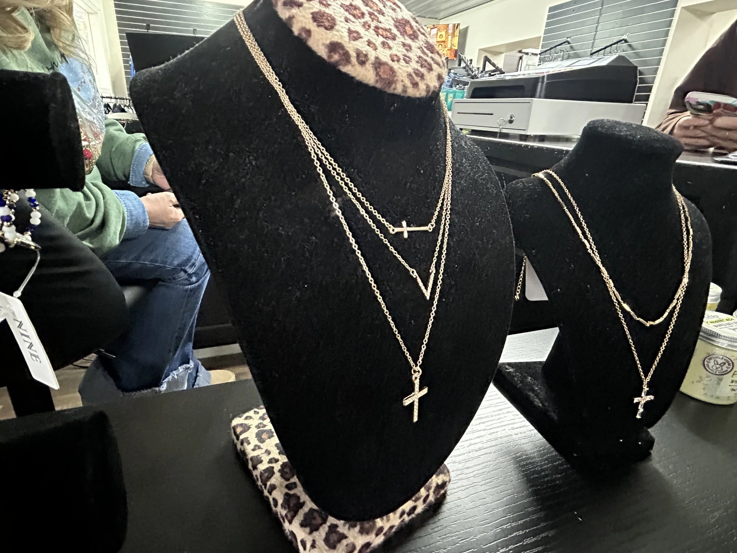 Display of layered gold necklaces with cross pendants on black velvet busts in the jewelry section.