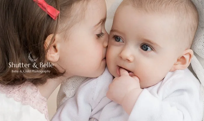 A young girl kissing her baby sister on the cheek