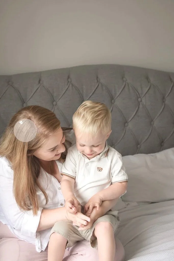 A woman and a young boy sitting on a bed sharing a moment of laughter and affection.Newborn, baby and family photography. Dublin.
