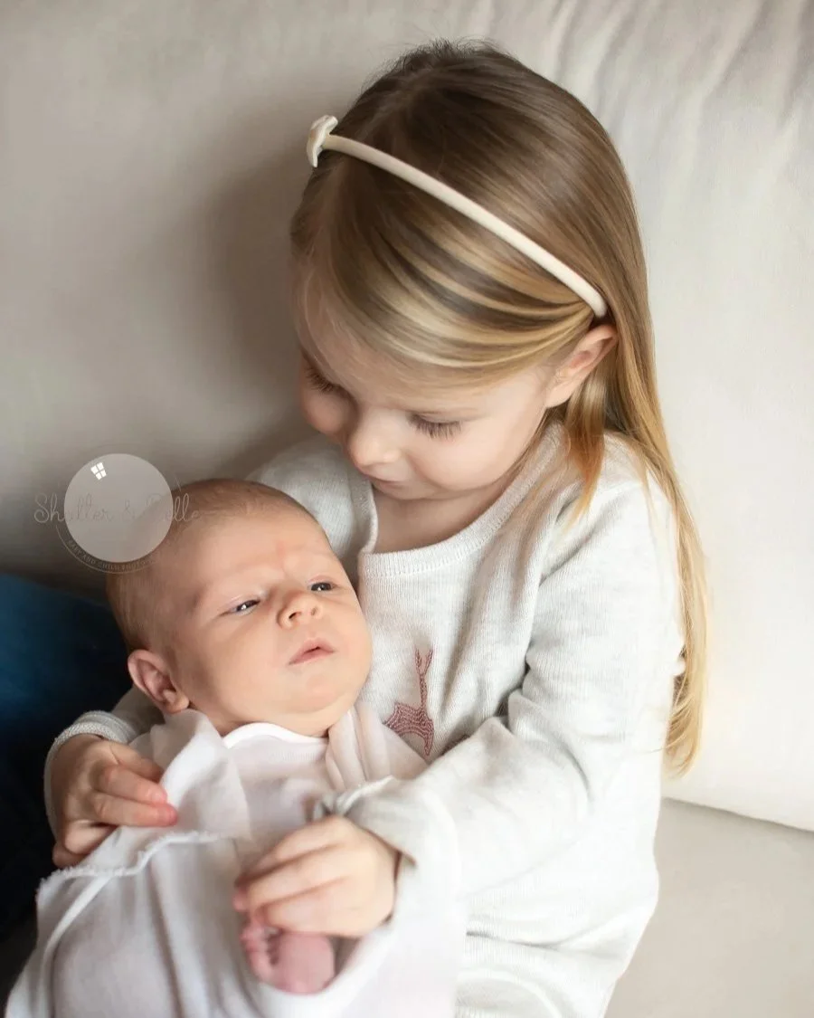 A young girl holding and looking at a newborn baby.