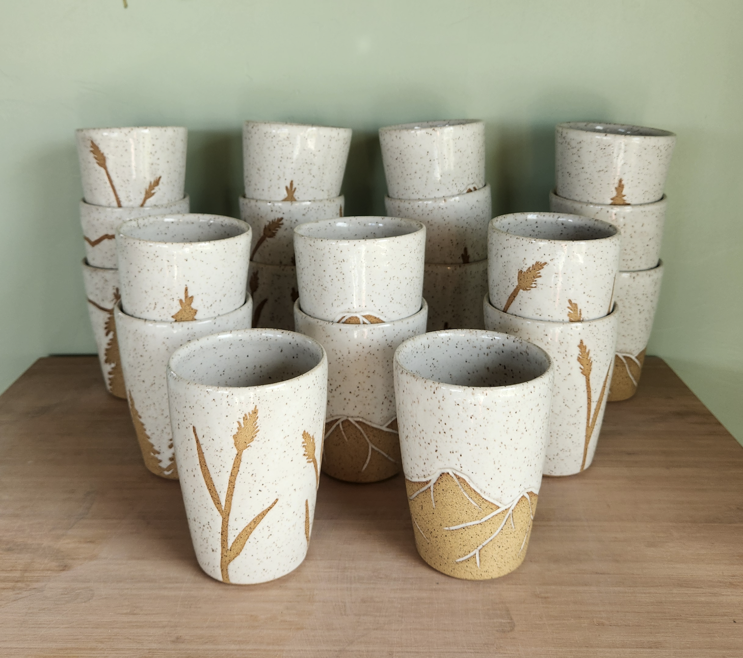 Stacked ceramic cups with nature designs on a wooden surface against a green wall.