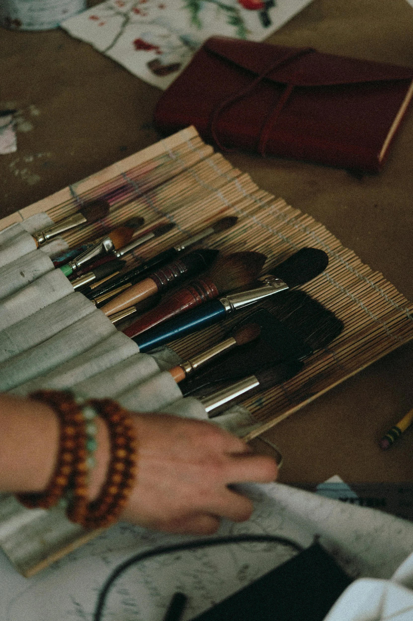 Viele, teilweise benutzte, Pinsel liegen auf einer Holzmatte.