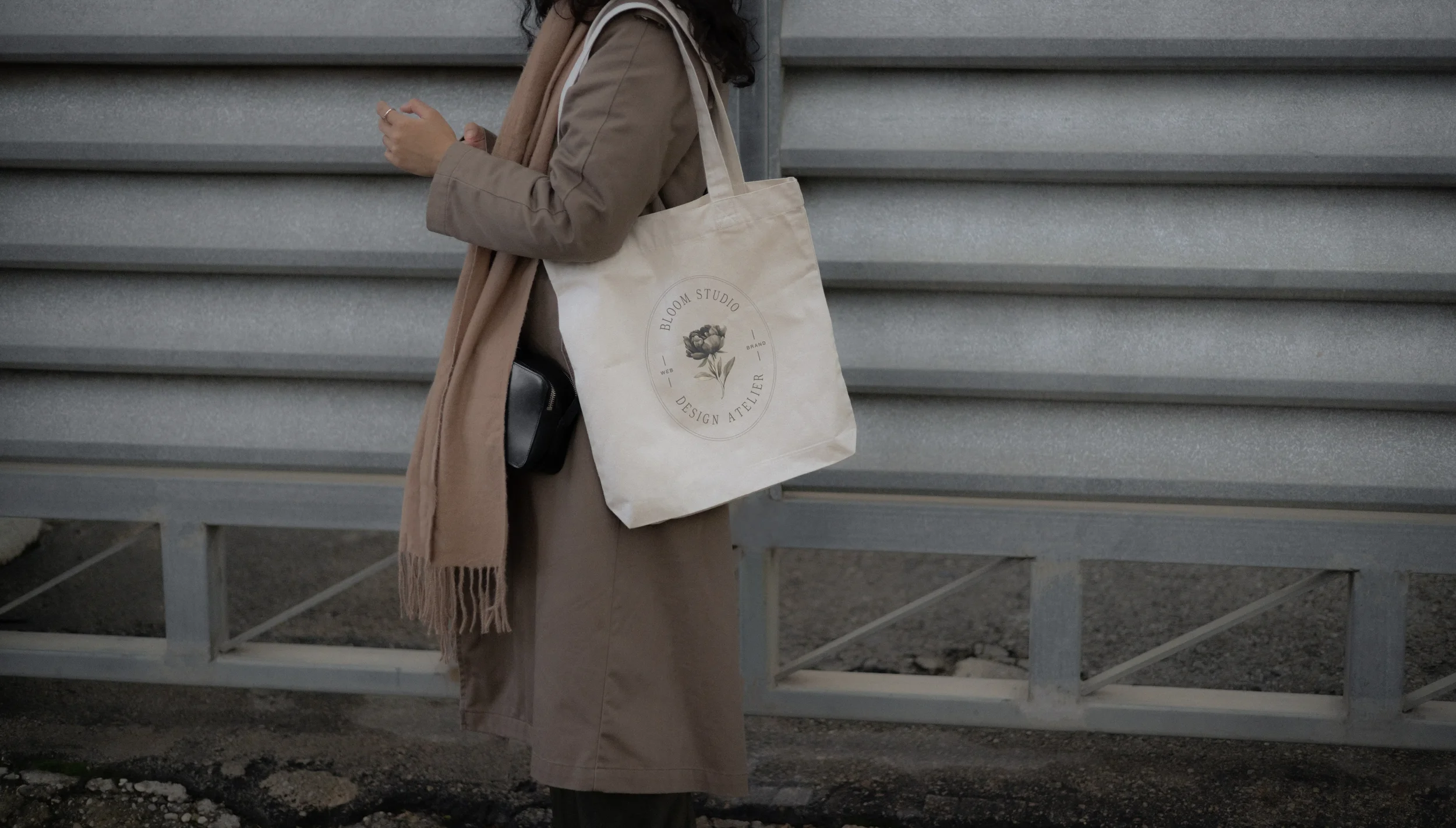 Eine Frau in braunem Mantel trägt eine Jutetasche mit dem Bloom Studio Logo drauf.