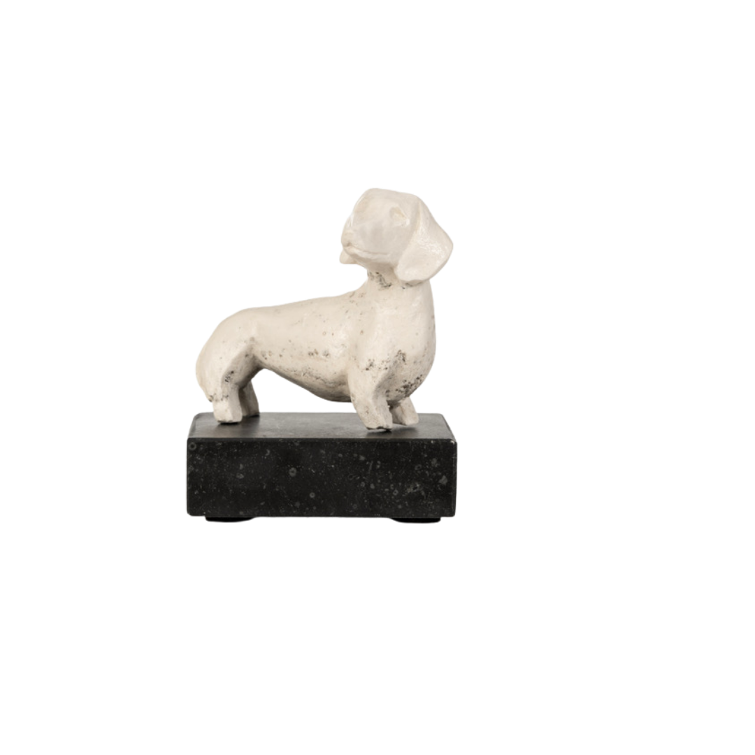 Een beeldje van een dier dat lijkt op een teckel, gemaakt van wit of licht gekleurd materiaal, geplaatst op een zwart granieten basis.