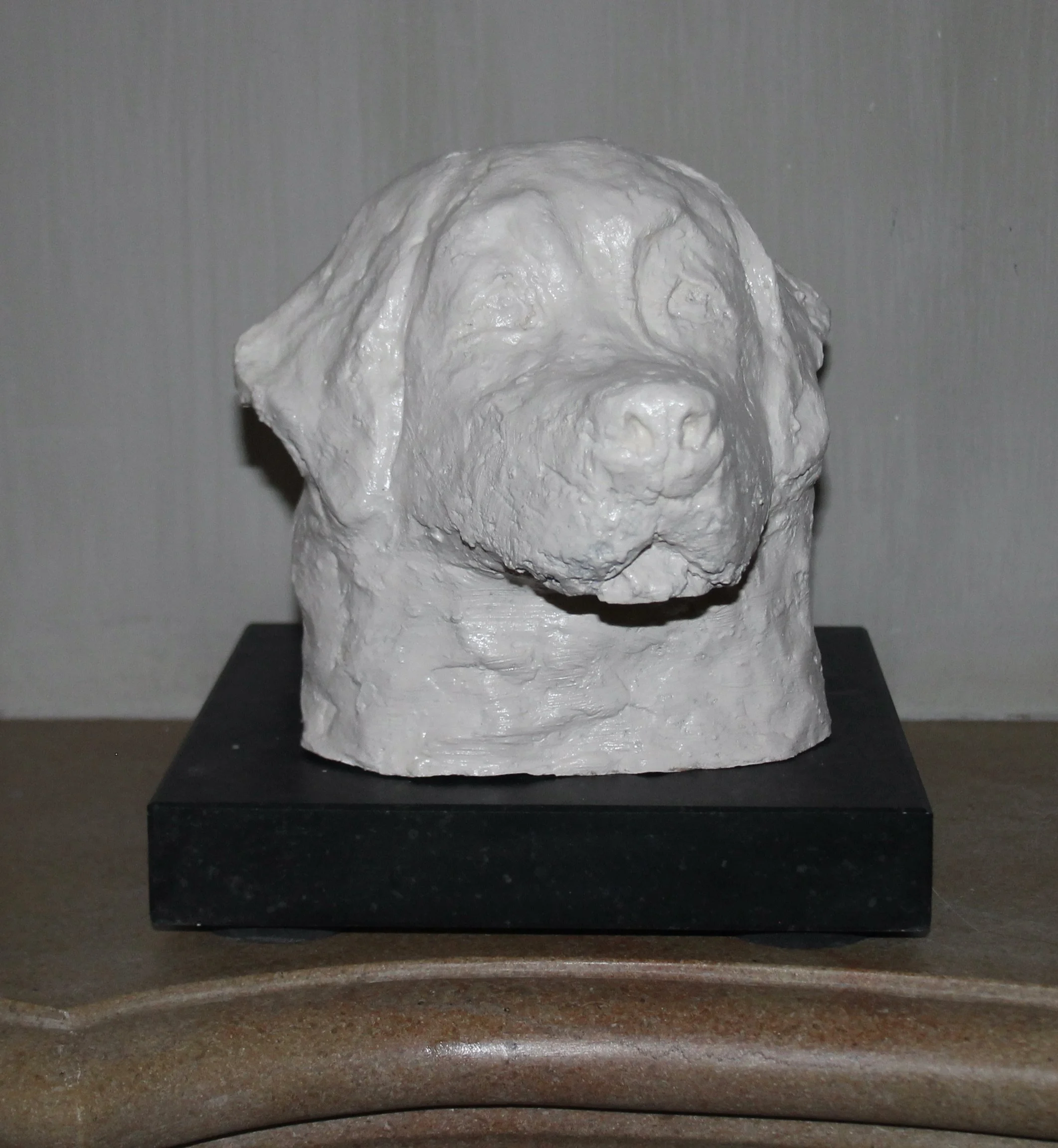 Een witte beeldhouwwerk van een hond, geplaatst op een zwarte sokkel.