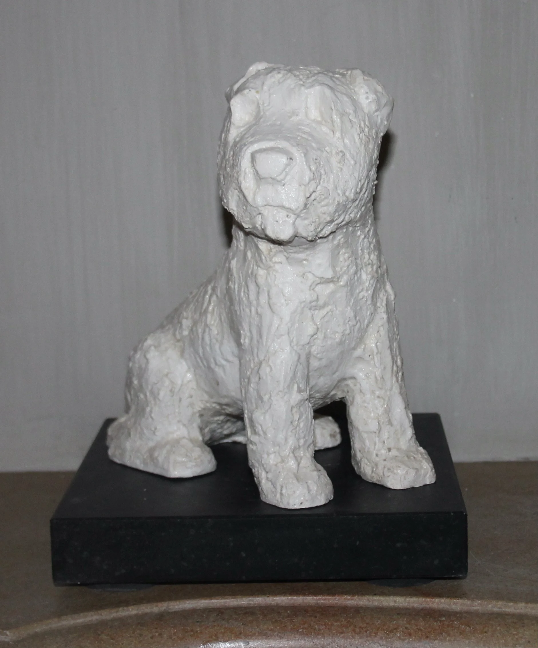 Witte beeldhouwwerk van een sitzende hond op een zwarte basis.