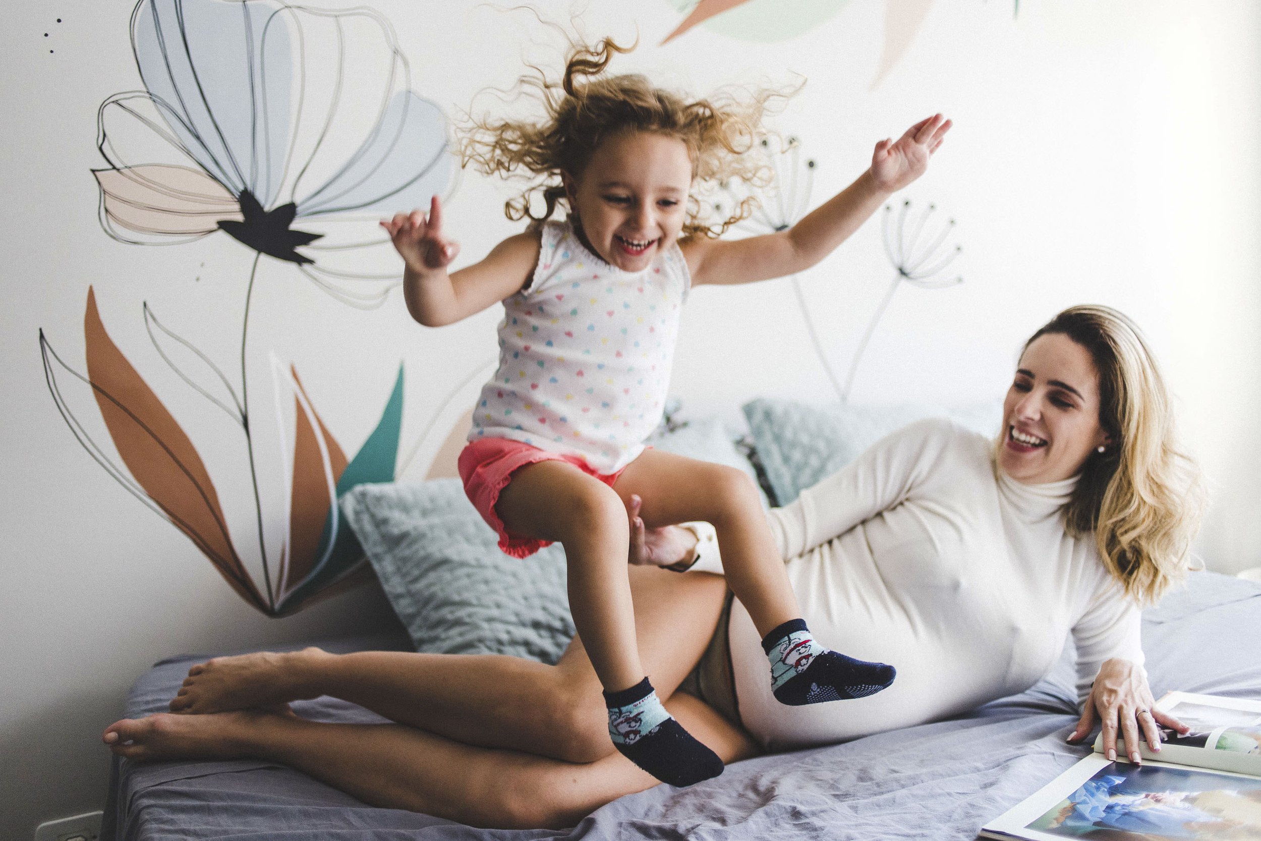 Lifestyle family photo of a woman and child jumping on a bed together during a playful at-home session.