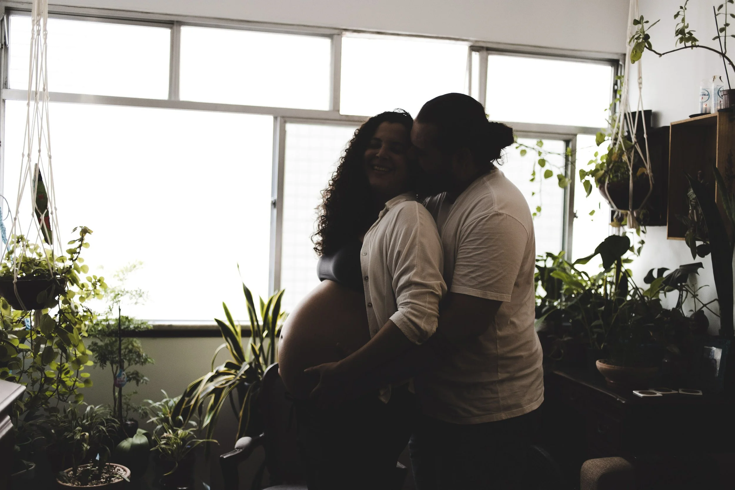 Pregnancy portrait of a couple sharing an intimate moment during an at-home maternity photo session surrounded by natural light and plants.