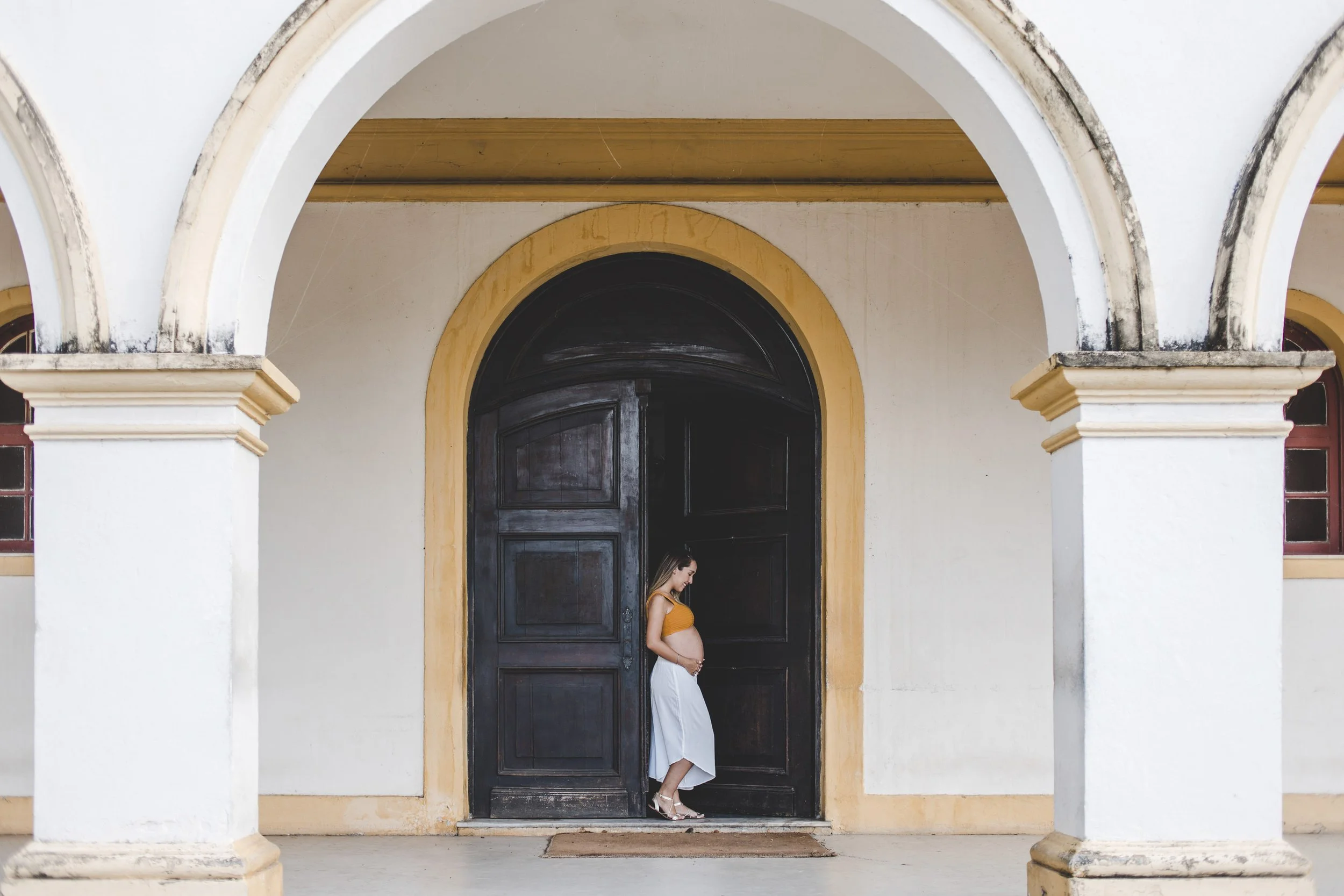 Pregnant woman photographed beneath architectural arches during an outdoor maternity session.
