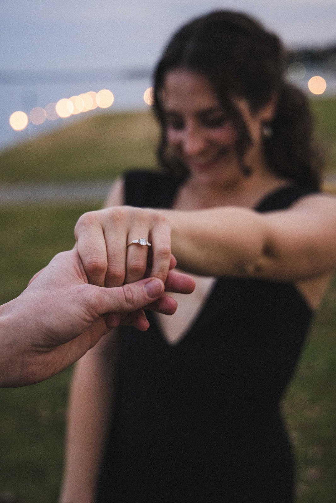 A woman showing her engagement ring while holding hands with her partner during an engagement photo session.