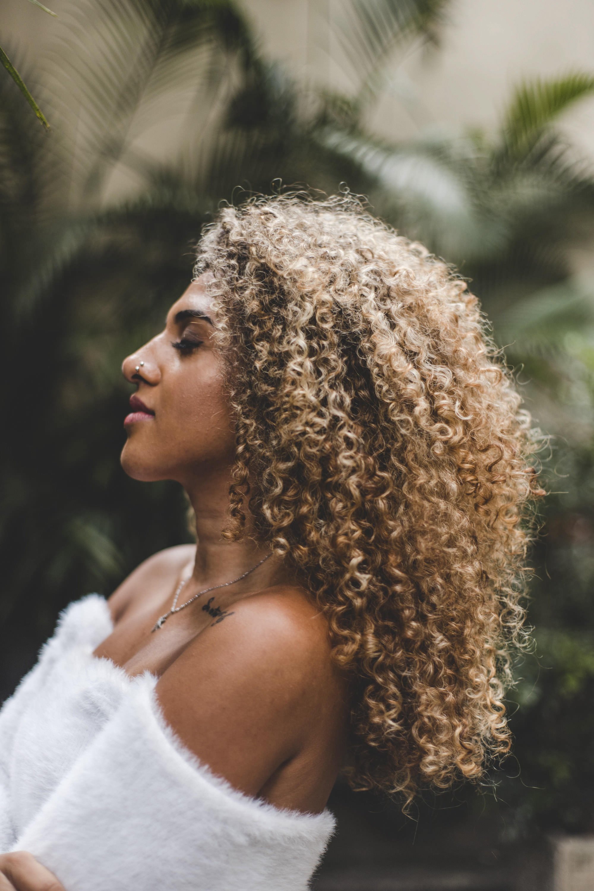Side-profile portrait of a singer and actress, Nat Barreto, with curly hair photographed outdoors in soft natural light.