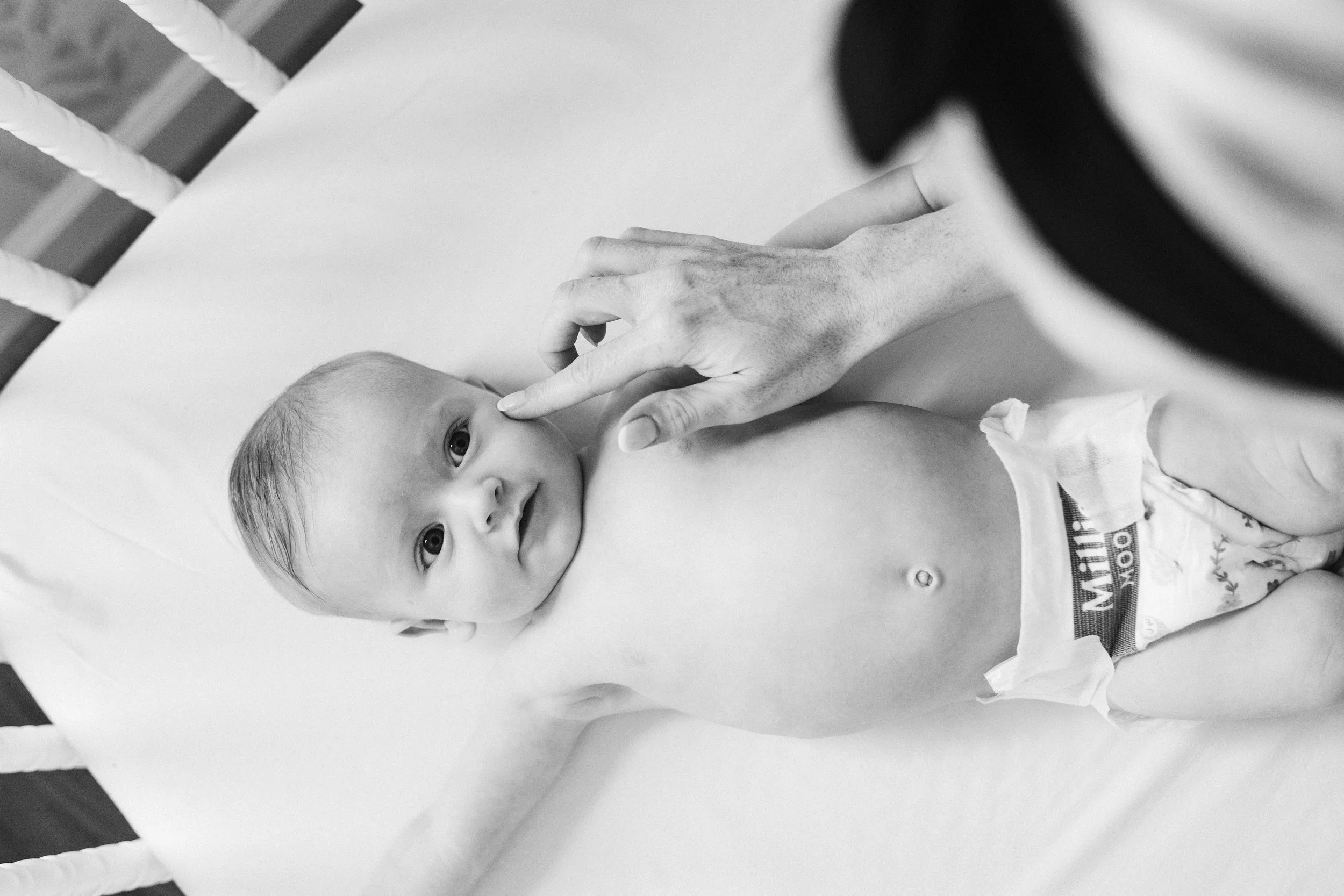 Lifestyle family photo of a baby lying on a bed while a parent gently touches the baby’s nose.