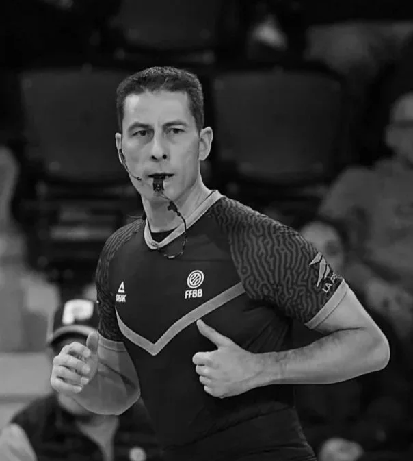 Arbitre de football en action, portant un maillot avec le logo FFBB, lors d'un match, en noir et blanc.