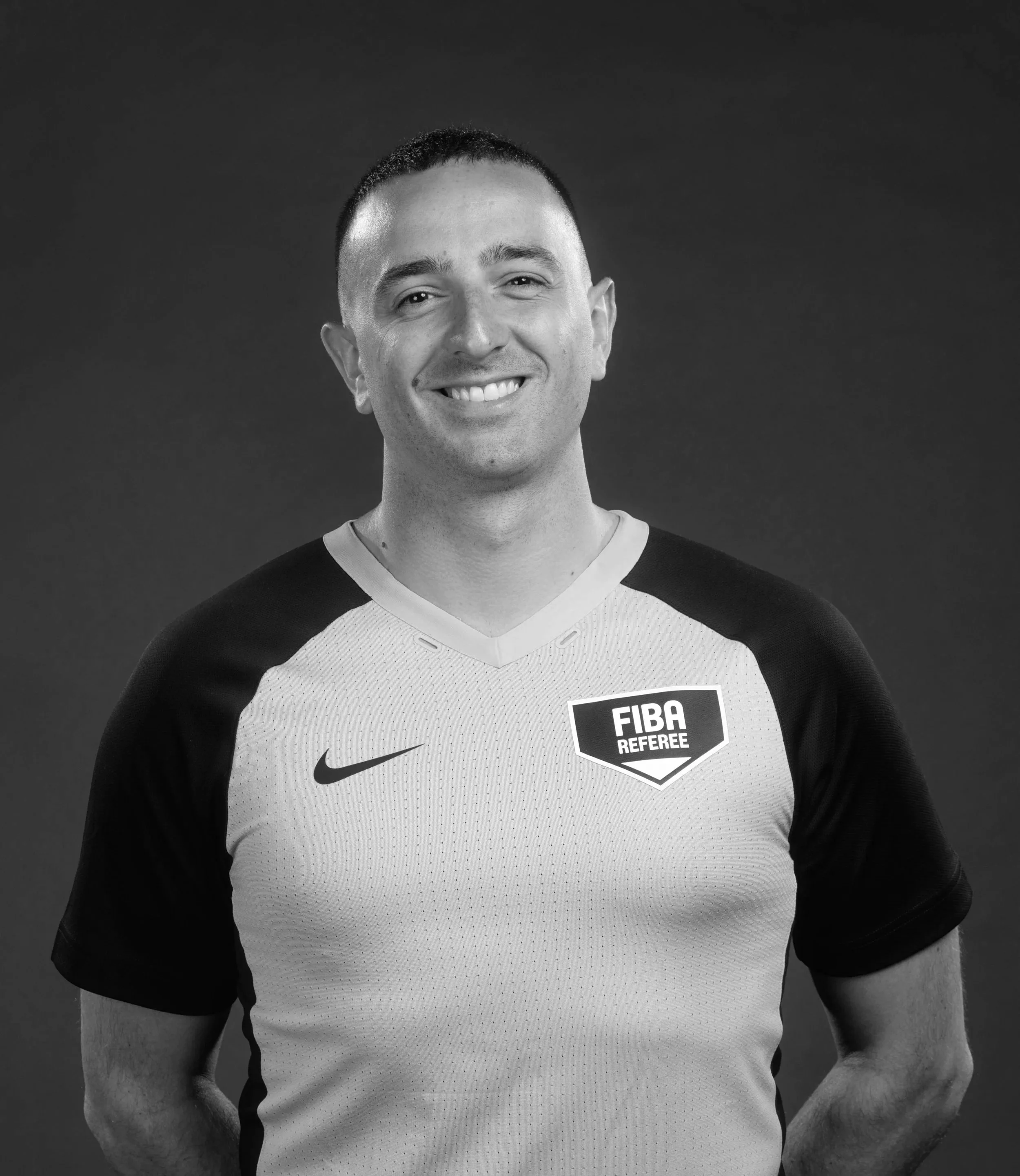 Un homme souriant porte un maillot de sport avec une étiquette FIBA arbitre sur la poitrine et le logo Nike