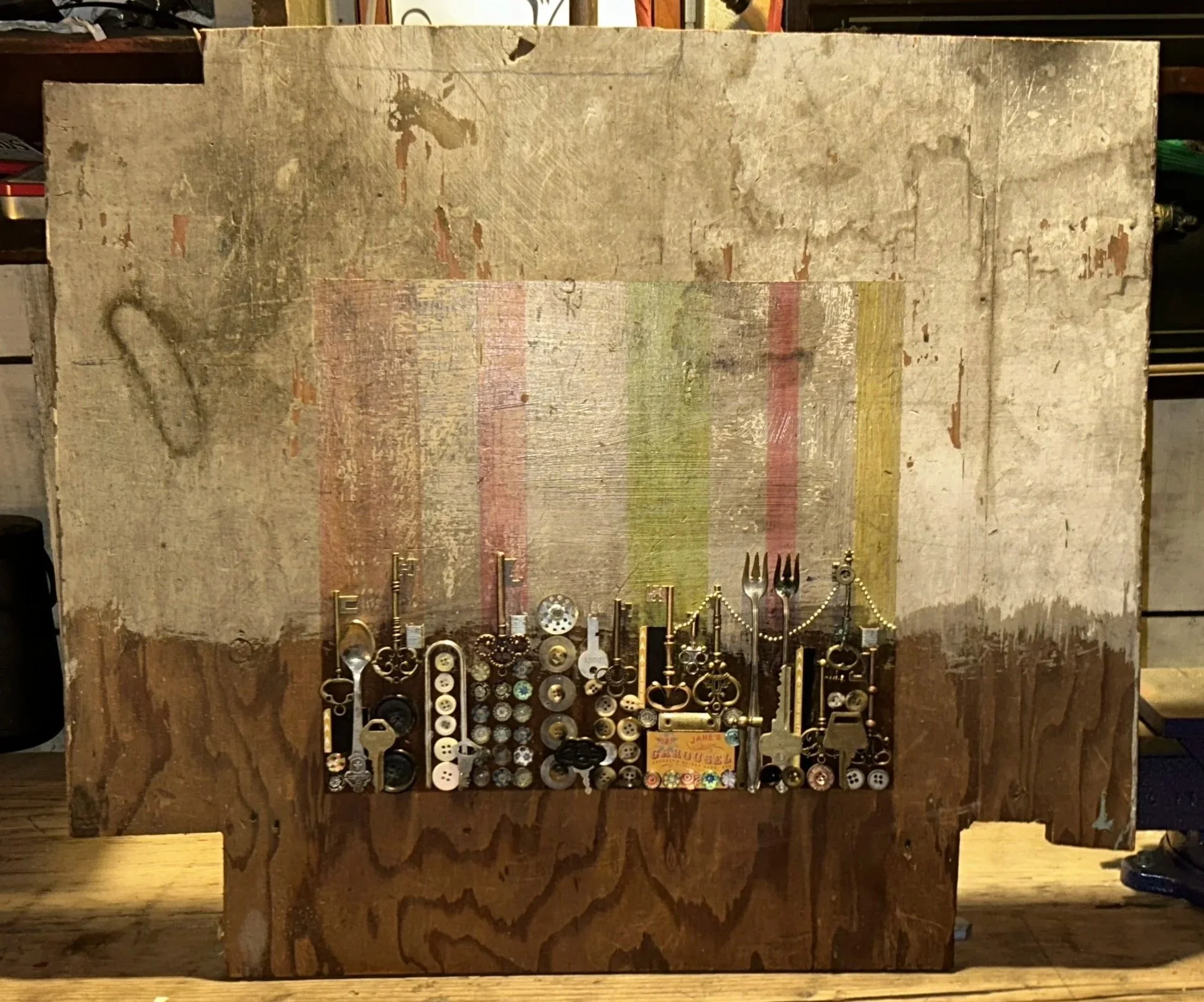 Canvas is an old 2 foot by 2 foot, irregularly cut square, with a cityscape of keys, buttons, and other metallic trinkets