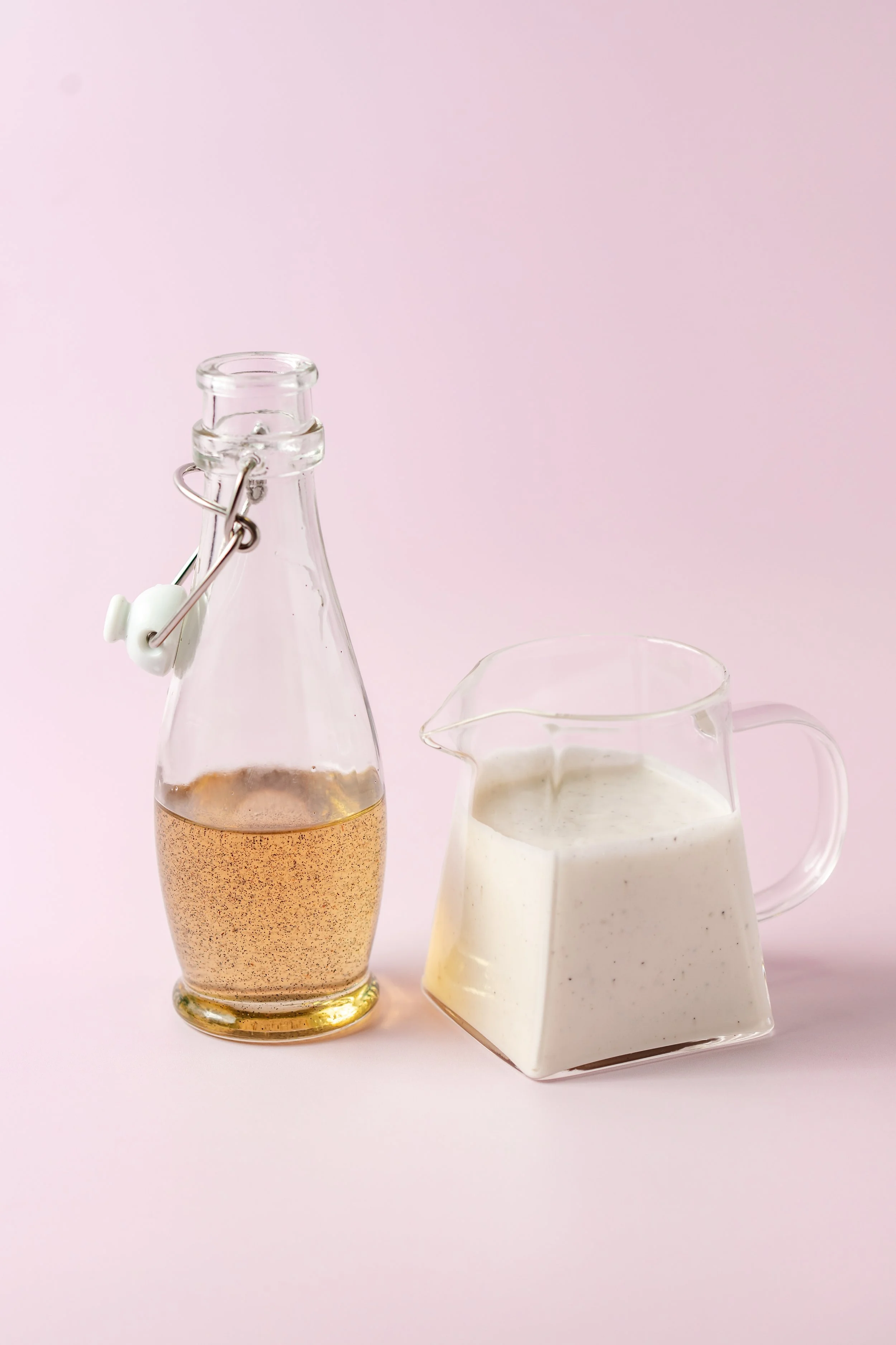 A glass bottle of sparkling apple cider and a pitcher of ranch dressing on a pink background.
