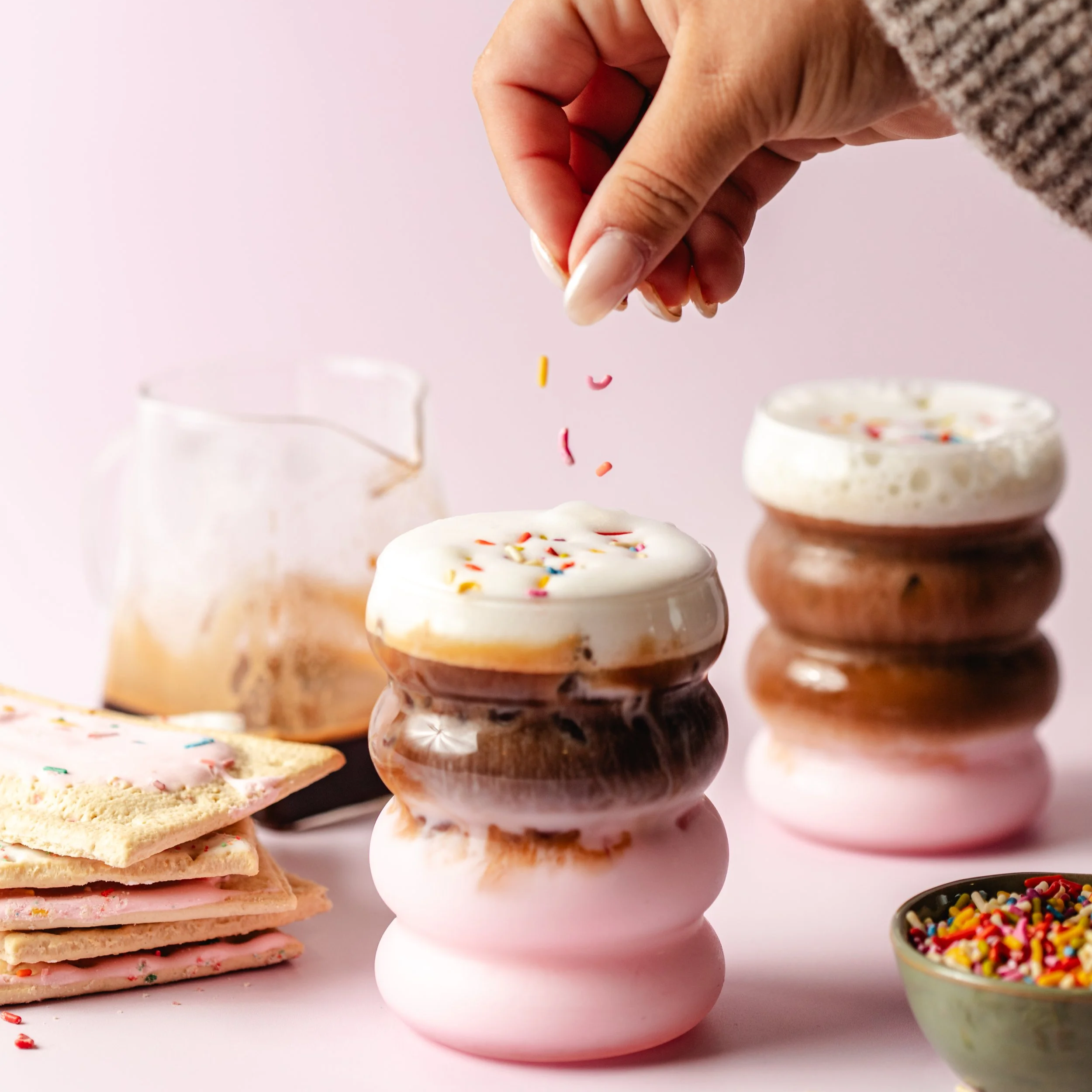 Hand sprinkling colorful sugar sprinkles onto a stack of iced cookies.