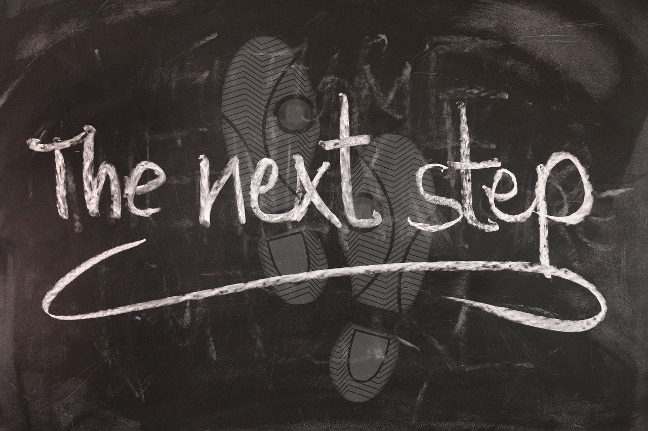 Chalkboard with the words "the next step" written in white chalk, with a footprint pattern in the background. Representing the next step being counselling services wtih Kristine.