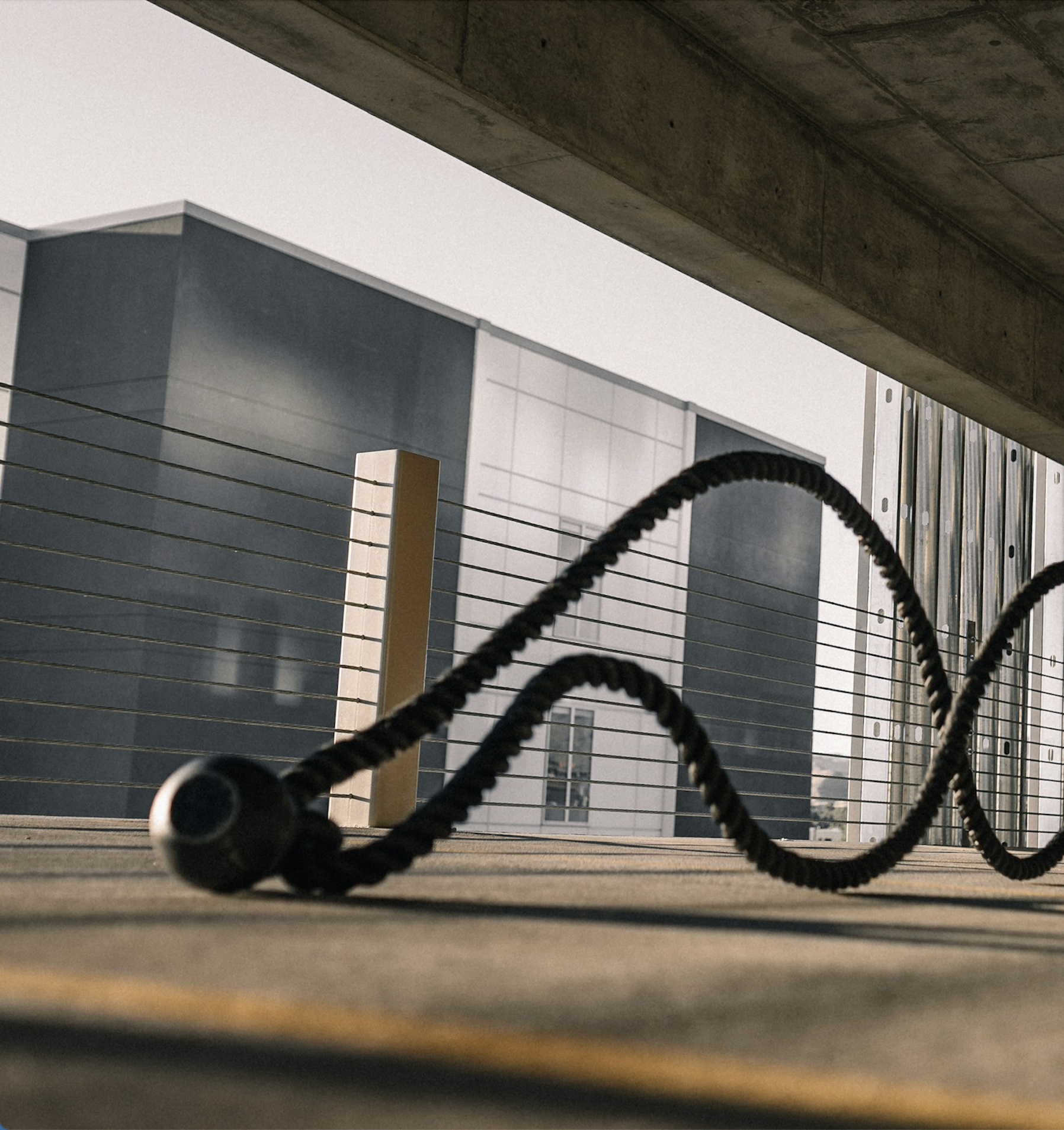 Close-up of a black rope with a handle on a rooftop with skyscrapers and cloudy sky in the background.