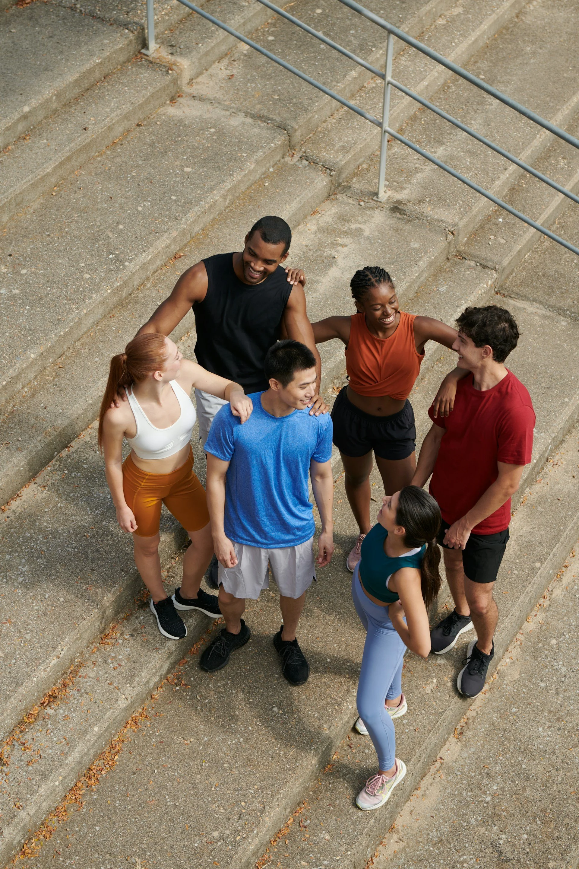 Group of six young adults standing on concrete stairs outdoors, smiling, and interacting with each other.