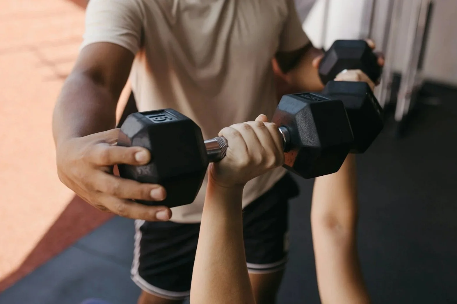 A person is helping a child do an overhead weightlifting exercise with a dumbbell at the gym.