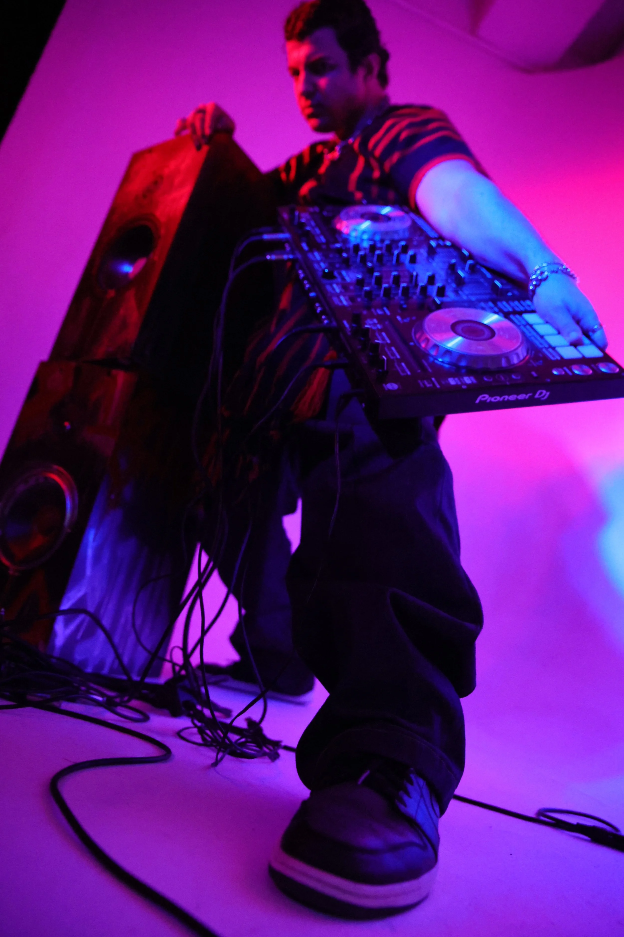 DJ playing electronic music on a Pioneer DJ controller with purple and pink lighting.