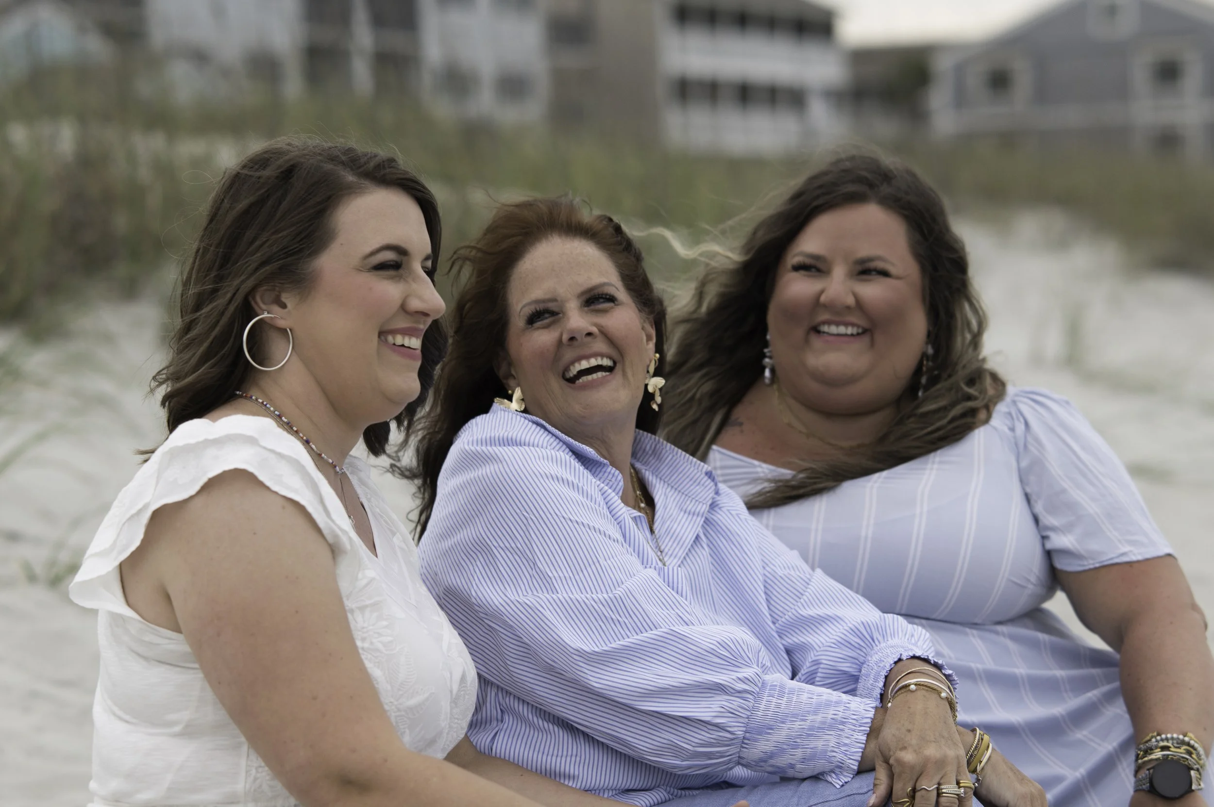 Three women sitting on the beach, smiling and laughing together during daytime.