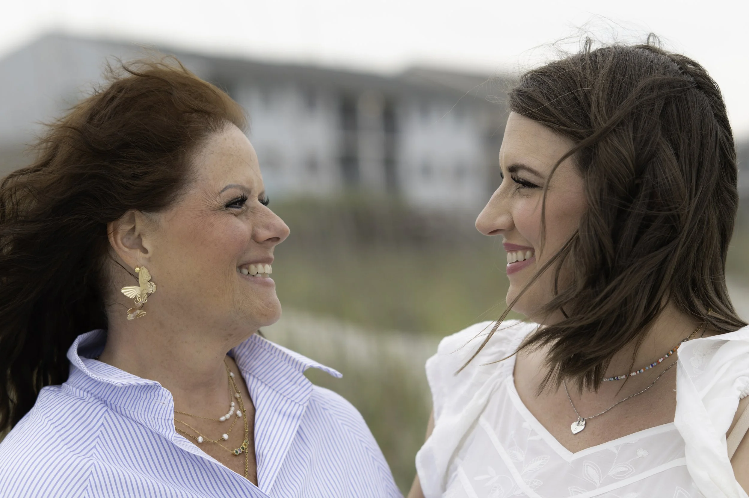Two women face each other closely outdoors, smiling, with blurred background